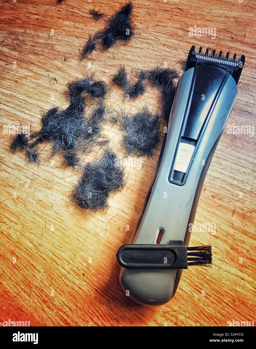 Un regolacapelli, una spazzola e tagli di capelli su pavimento in legno. Foto Stock