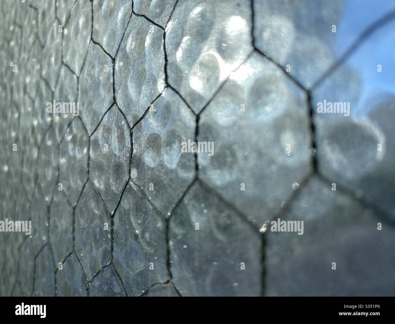 Vista angolata del vetro di sicurezza opaco con rete metallica che lo attraversa. Fuoco poco profondo e forme indistinte visibili attraverso di esso, creando una trama astratta di sfondo. Foto Stock