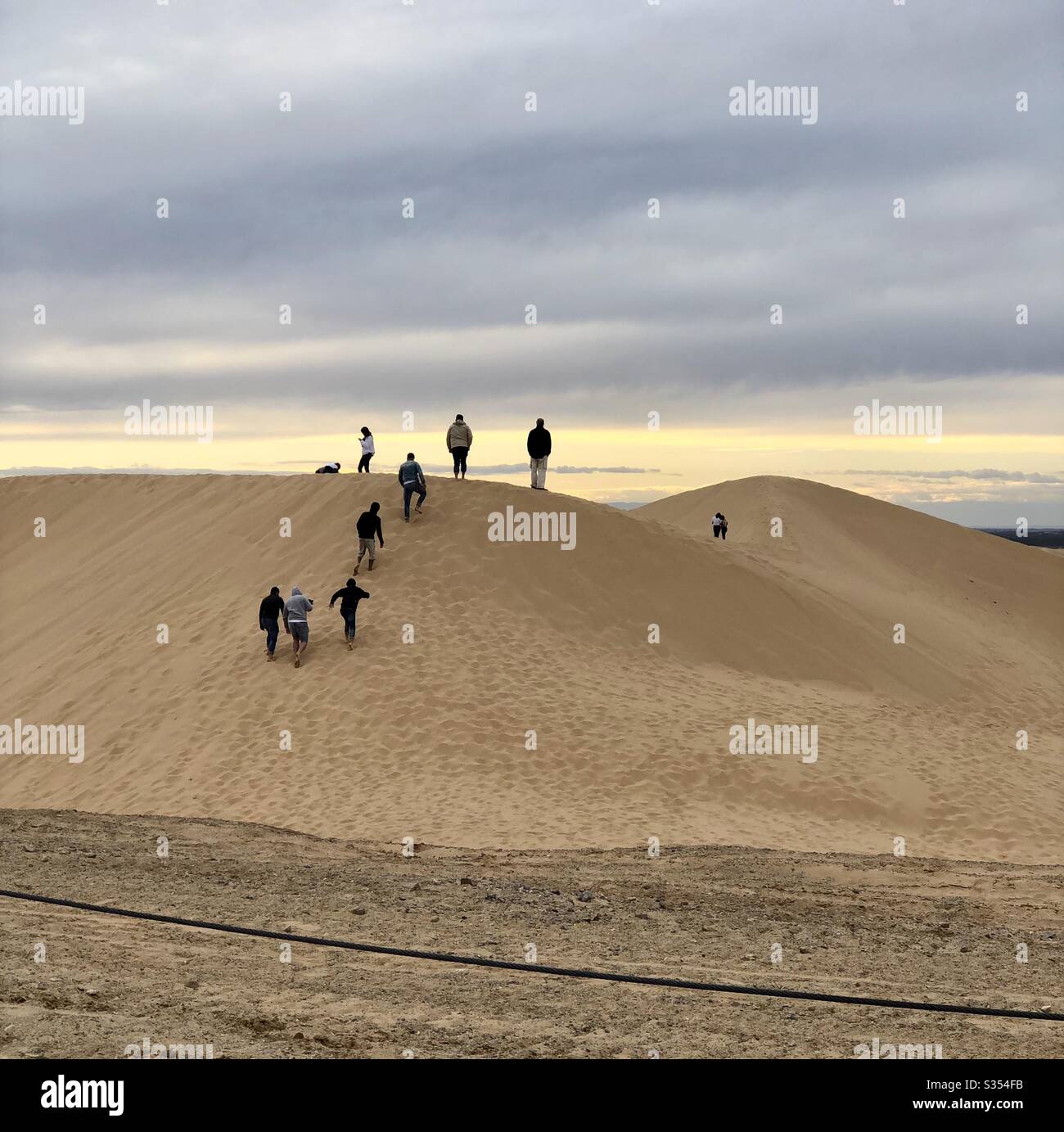 Undici persone inidentificabili, arrampicata, dune di sabbia, cielo nuvoloso, tardo pomeriggio, attività, esercizio fisico, insieme, godersi la vita, momenti di divertimento, attività all'aperto, natura Foto Stock