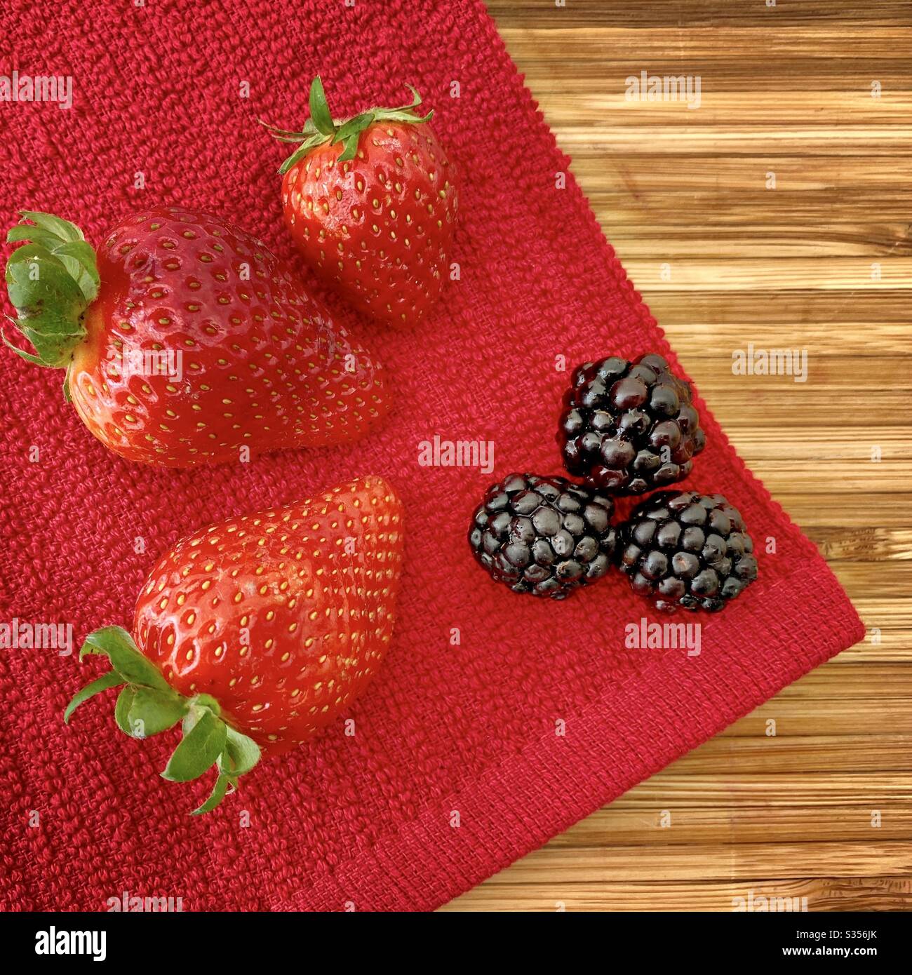 Fragole e more su un banco da cucina in legno. Ingredienti per cuocere una torta di frutti di bosco, fragole e mora. Foto Stock