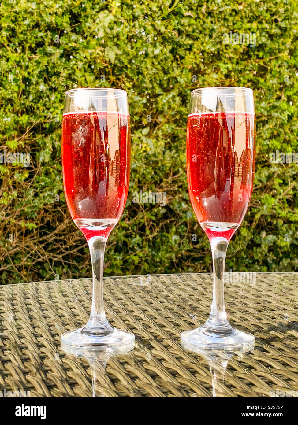 Due bicchieri di flauto di champagne rosa sulla parte superiore di un tavolo in giardino in una serata estiva Foto Stock