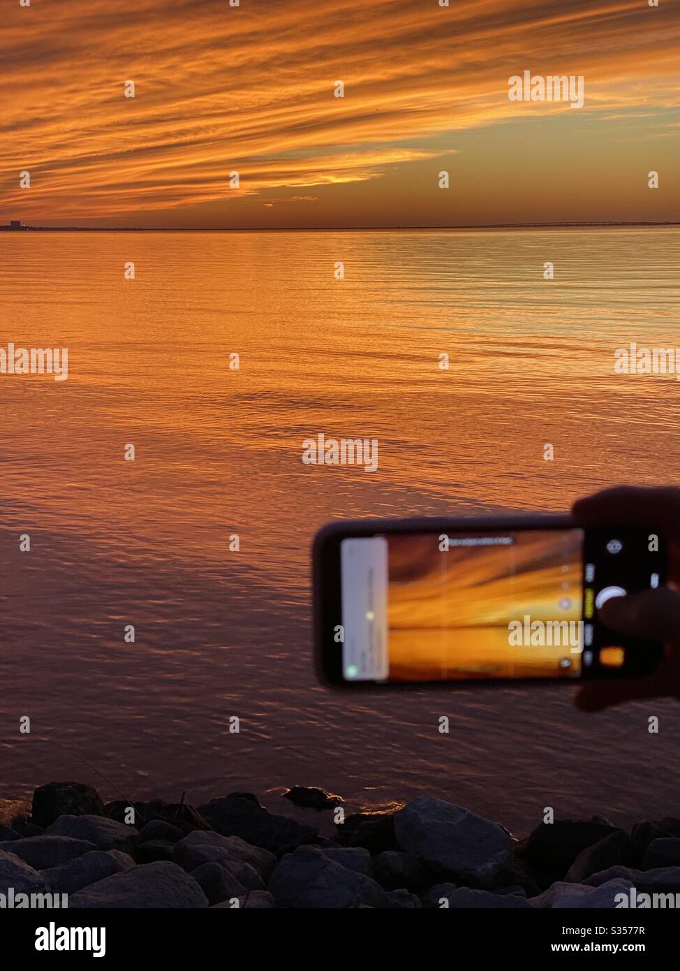 Tramonto luminoso sopra la baia di Choctawhatchee con un colpo sfocato dei miei amici iPhone che scatta le foto del tramonto Foto Stock
