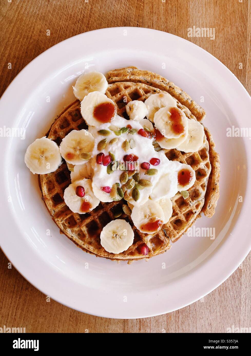 Un waffle per colazione, con fette di banana, yogurt, salsa di fragole, semi di zucca e semi di melograno. Foto Stock