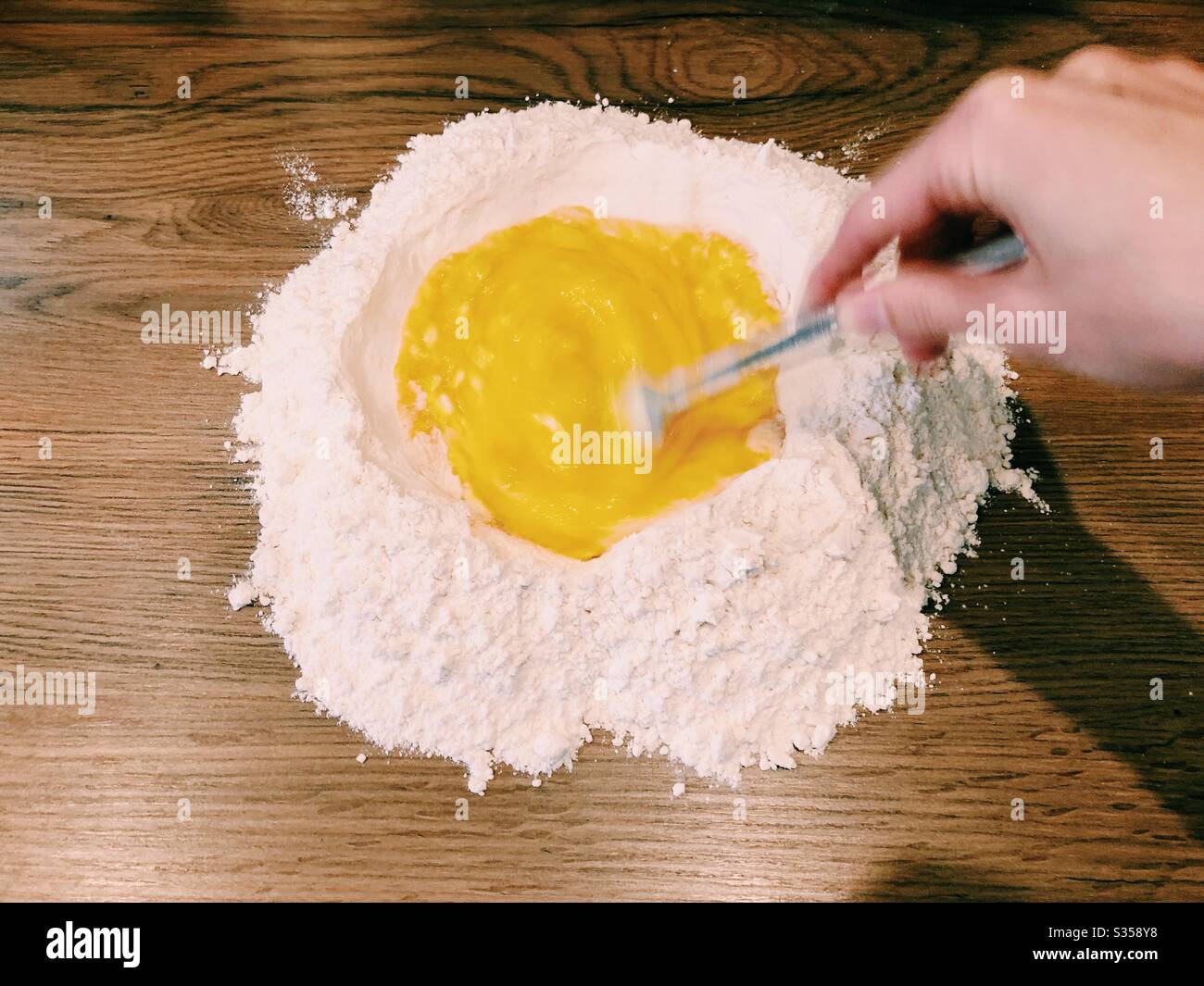 Mescolare le uova con le mani nella farina per preparare la pasta Foto Stock