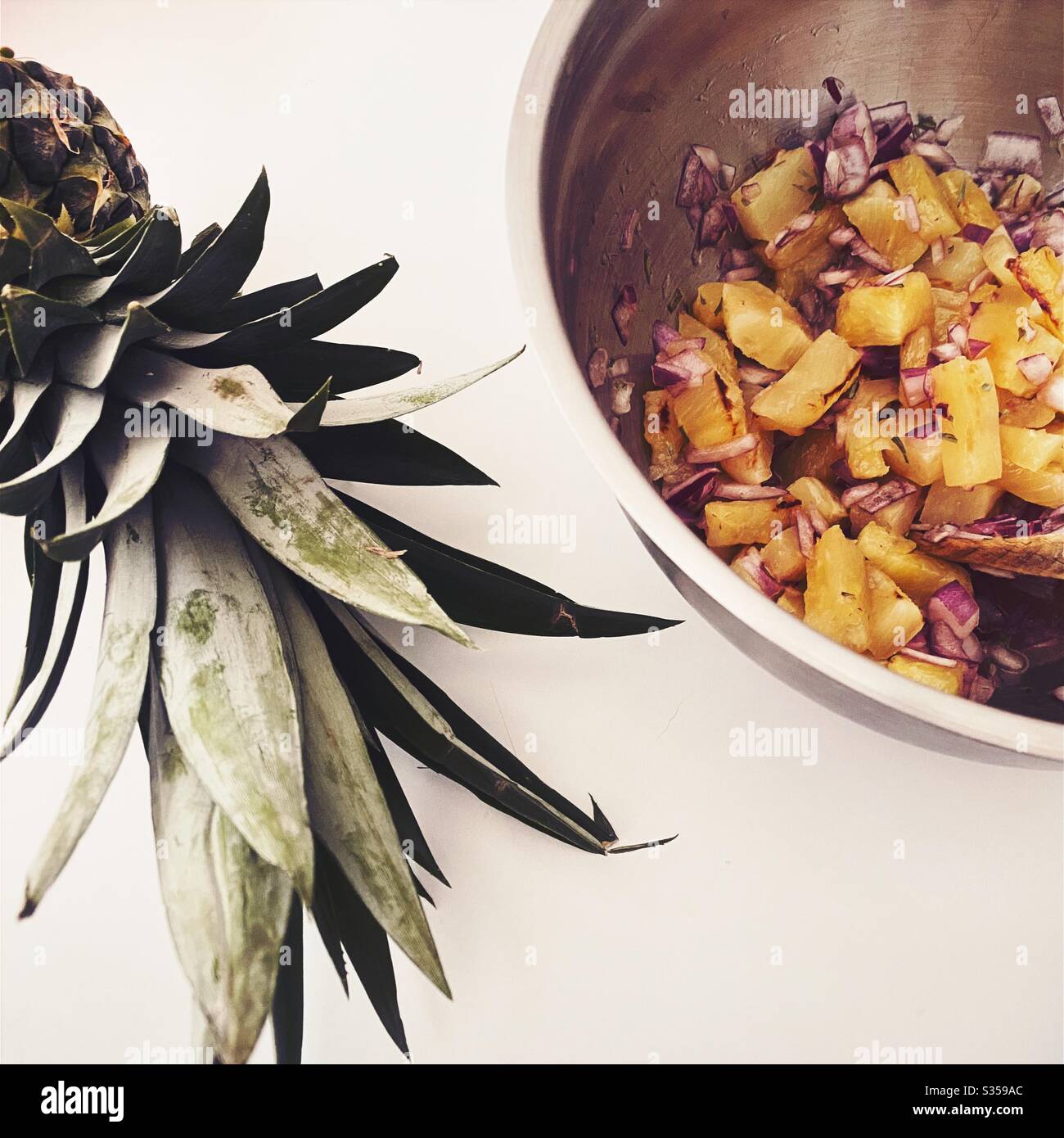Preparazione di un piatto di ananas in cucina. Preparazione di frutta fresca e matura. Ingredienti per la salsa di ananas fatta in casa. Pezzi alla griglia con cipolla rossa, succo di lime e coriandolo in una terrina di acciaio. Foto Stock