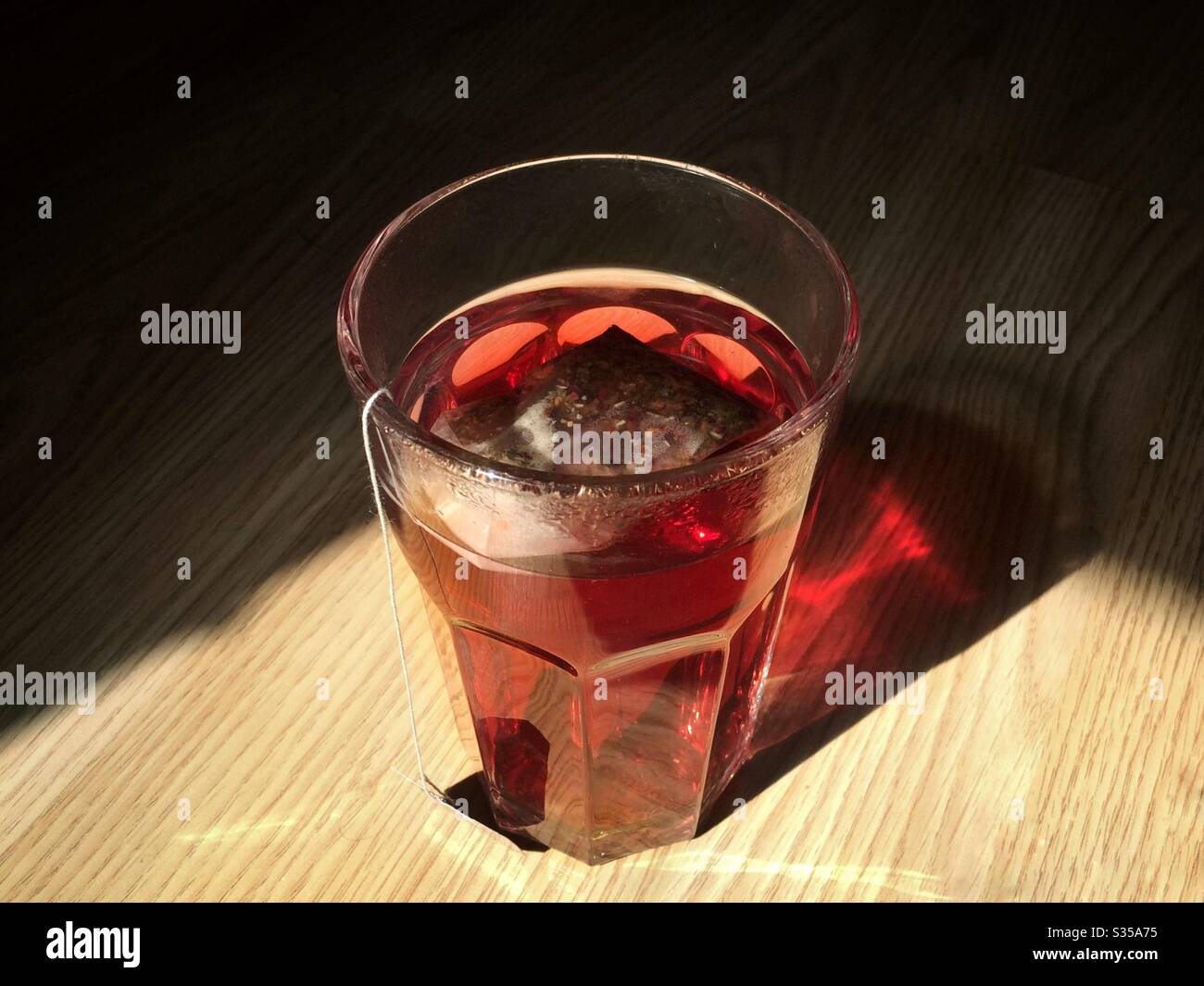 Un bicchiere di tè alle erbe su una superficie di legno con ombre dietro di essa Foto Stock