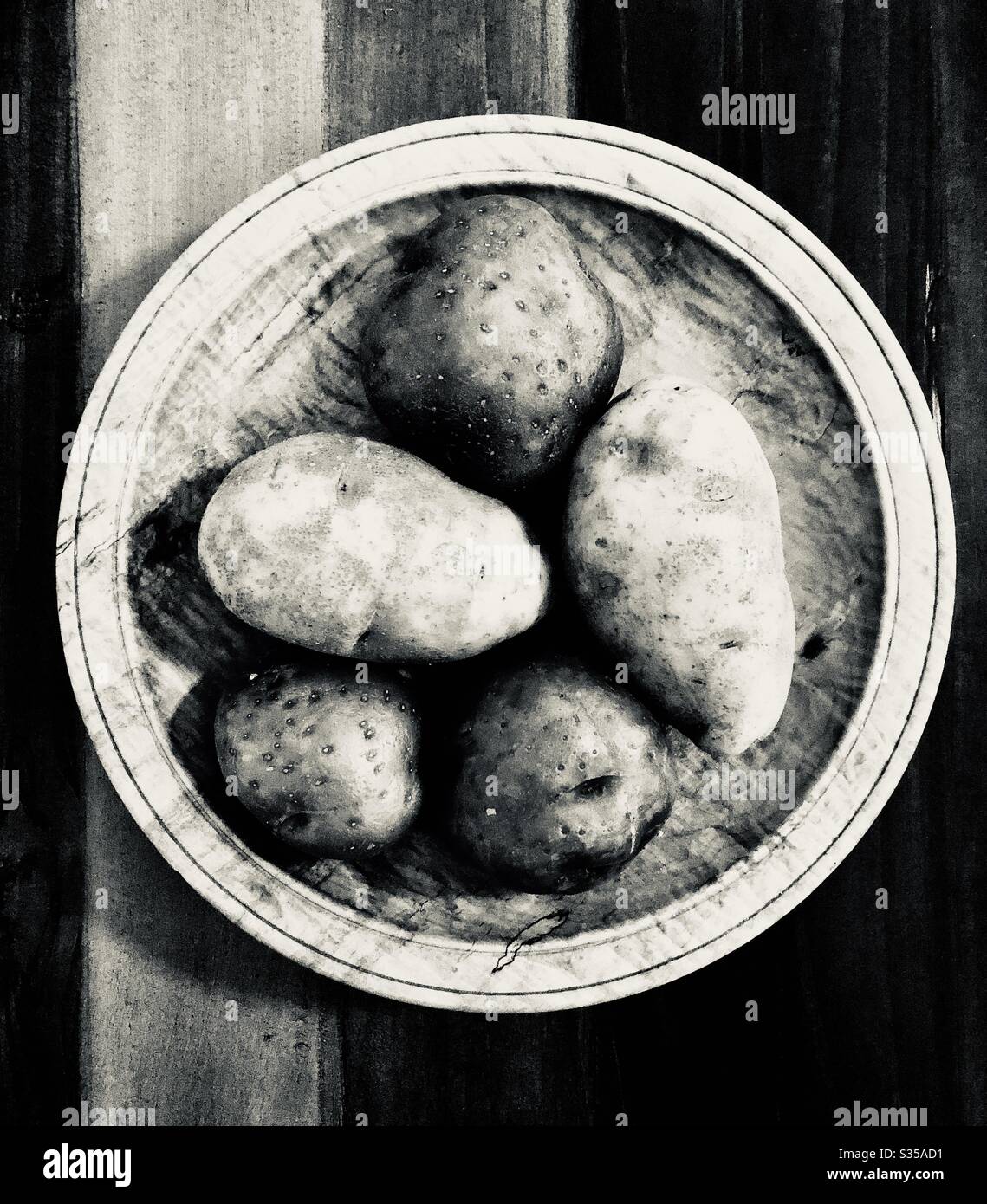 Foto monocromatica di patate 5’ su una ciotola e un tavolo di legno. Foto Stock