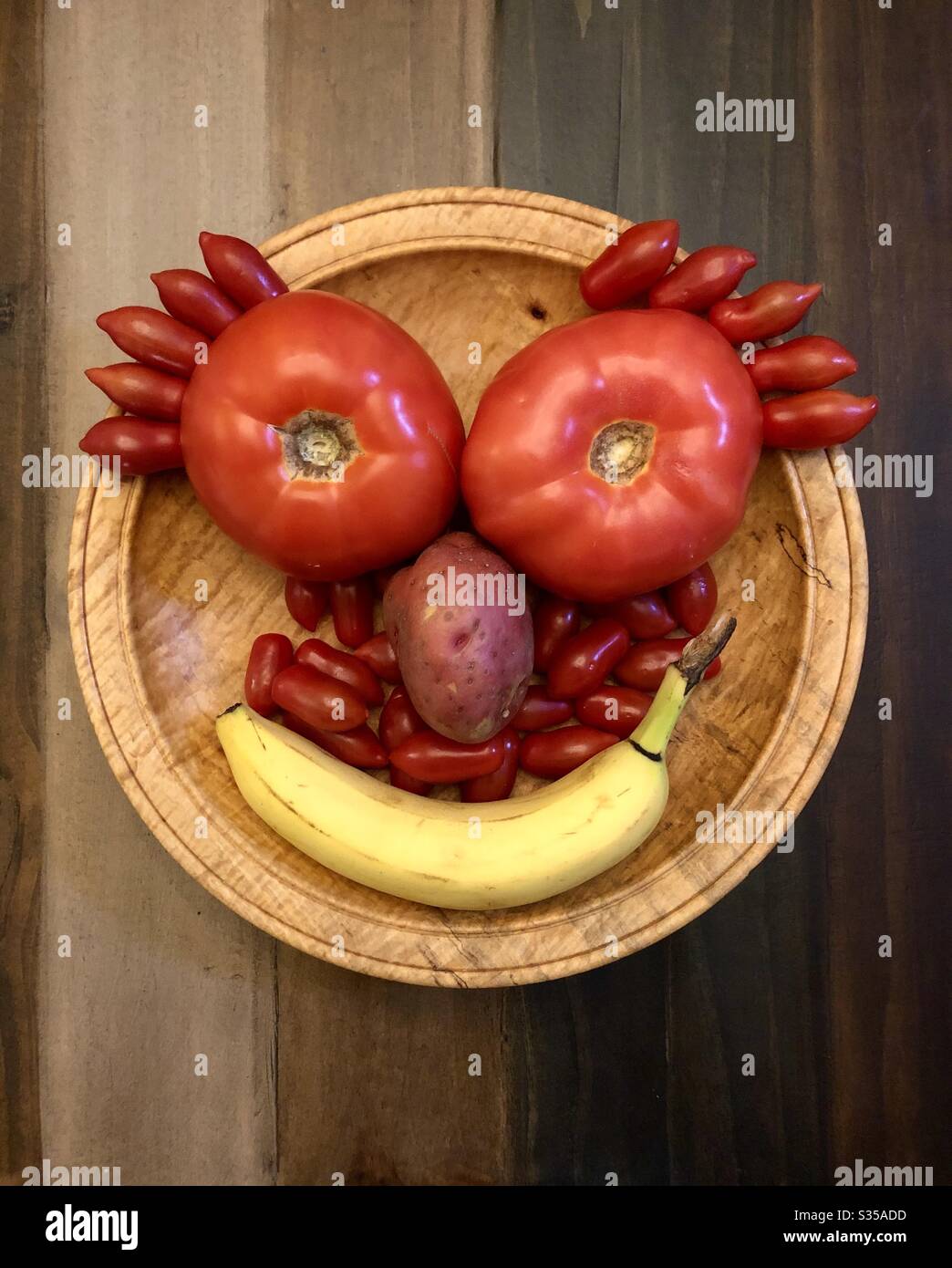 Faccia felice fatta di verdure e frutta su una ciotola di legno e piano del tavolo. - Immagine stock catturata con smartphone