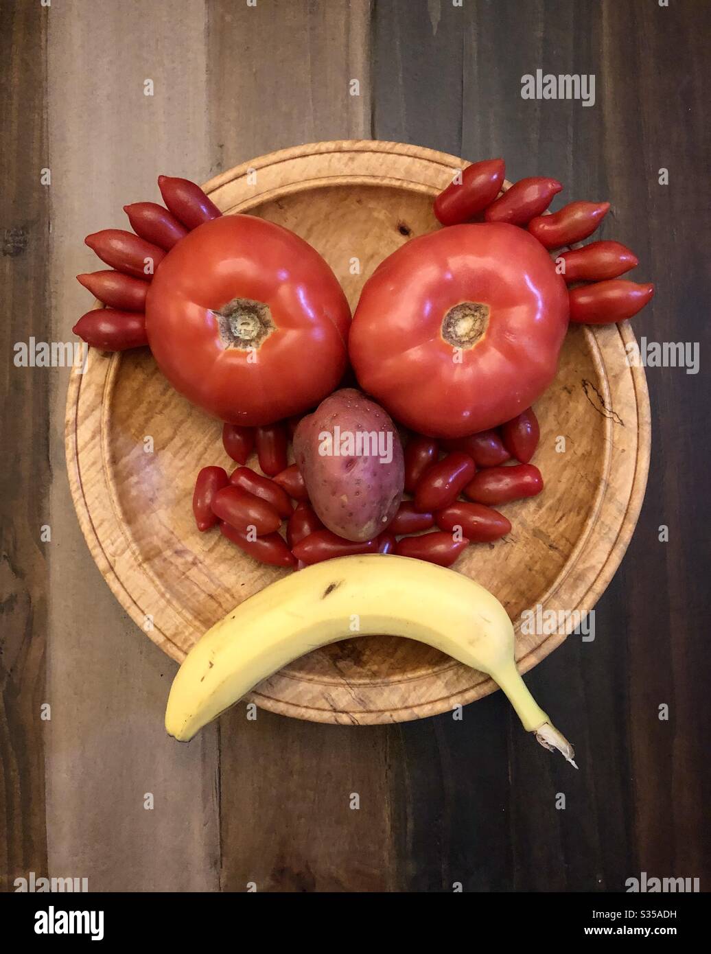Triste faccia composta di verdure e frutta in una ciotola di legno e su un tavolo. - Immagine stock catturata con smartphone