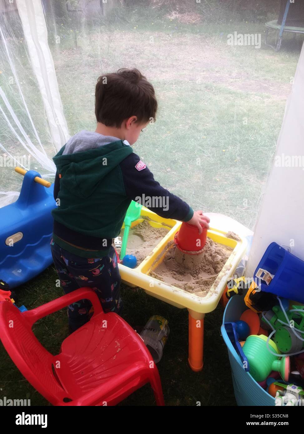 Toddler che fa i castelli di sabbia in piccolo tavolo di sabbia gialla Foto Stock