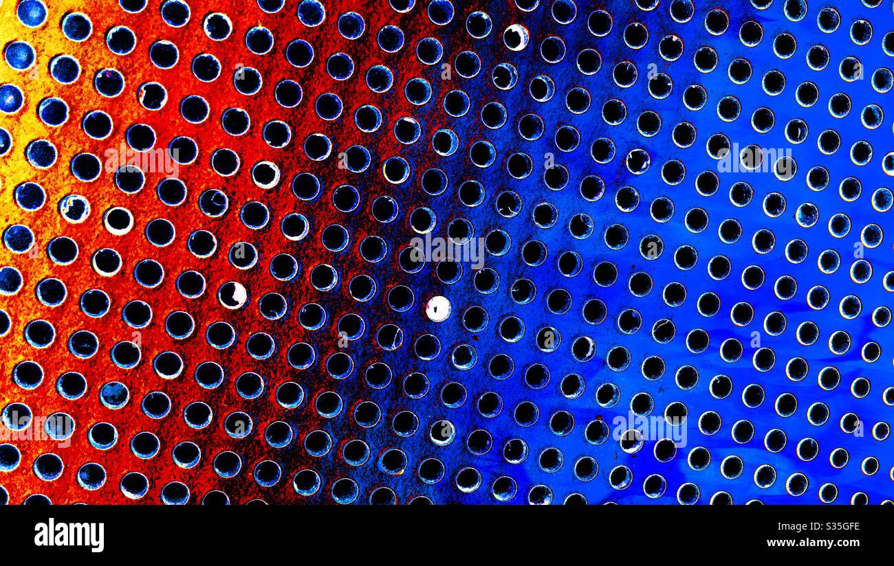 Immagine astratta di primo piano di una superficie metallica perforata rossa, gialla e blu, con graduali variazioni di colore Foto Stock