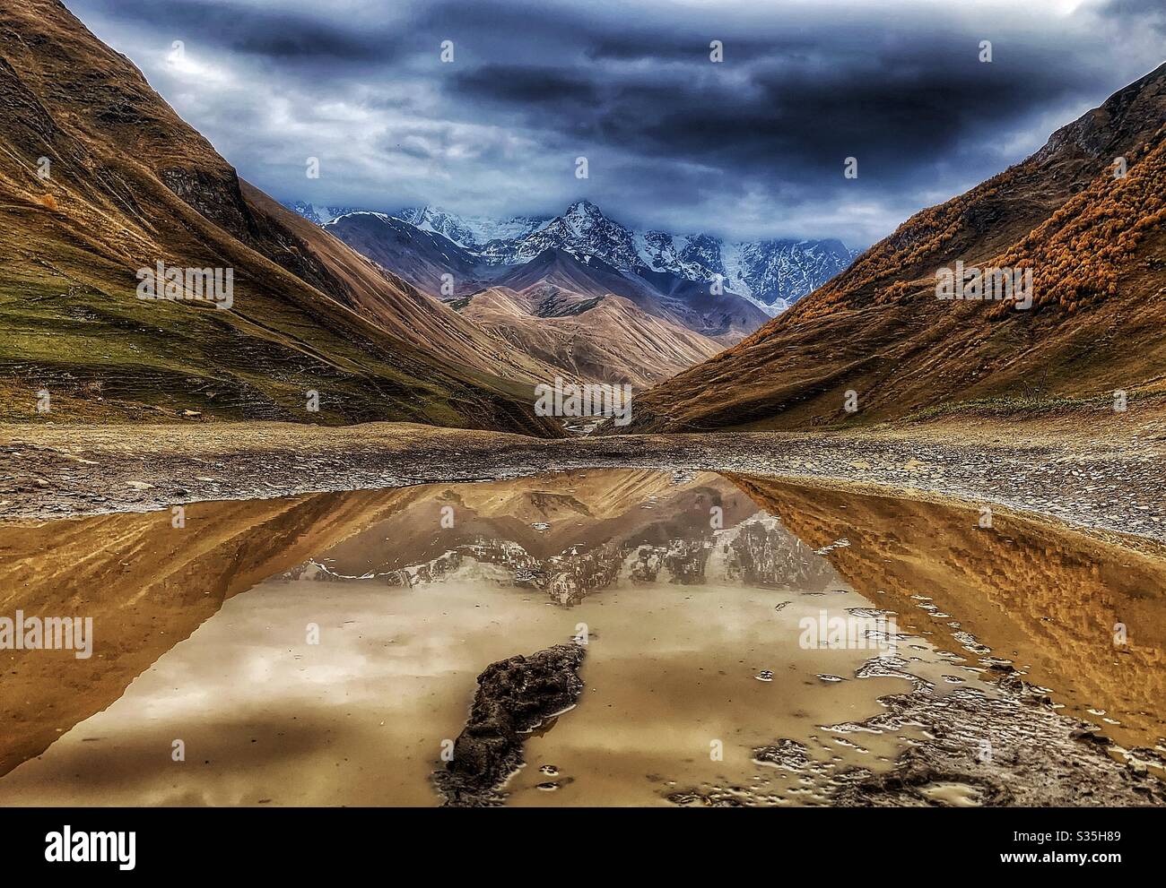 Riflesso di montagna nevoso in un pouddle a Ushguli, Georgia. - Immagine stock catturata con smartphone