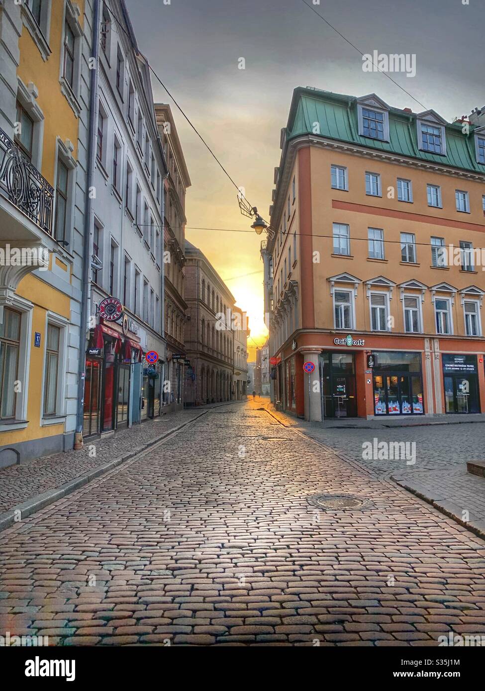 Città vecchia di riga, il sole sorge tra insoliti edifici colorati, con il bagliore del sole che mette in risalto la strada acciottolata. Foto Stock