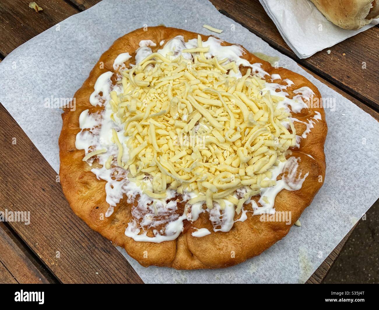 Langos Ungherese (pane fritto) ricoperto di panna acida e formaggio grattugiato. Su un tavolo di legno. - Immagine stock catturata con smartphone