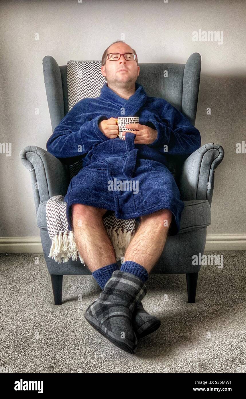 Domenica rilassante: Uomo che riposa in una poltrona grigia Ikea con una  medicazione blu e ciabatte grigie, in possesso di una tazza di caffè Foto  stock - Alamy