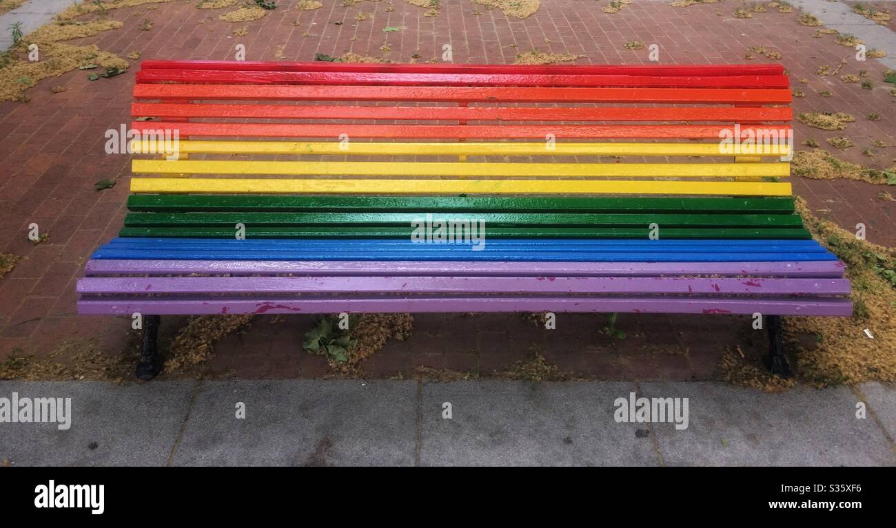 Panca dipinta in colori arcobaleno in strada Foto Stock