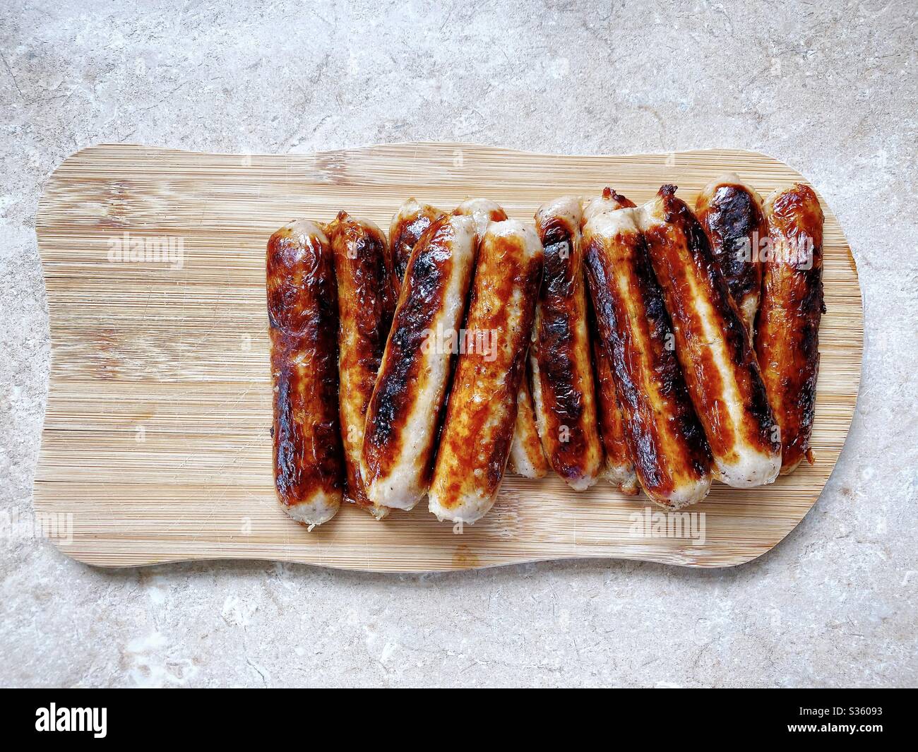 Vista dall'alto delle salsicce britanniche fritte della Cumberland su un tagliere in legno in cucina. Preparare la colazione a casa con carne cotta. Copia spazio a sinistra. Foto Stock