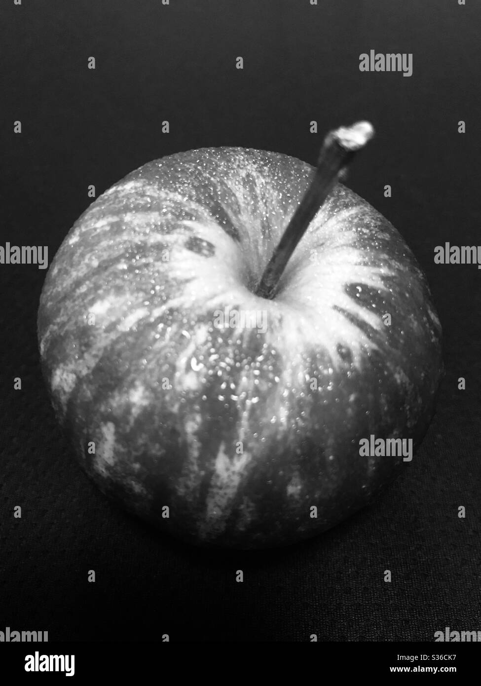 Il suggestivo aspetto bianco e nero di una mela rossa con gocce d'acqua dopo essere stata tenuta fuori dal frigorifero prima del consumo "una mela al giorno tiene lontano il medico" Foto Stock