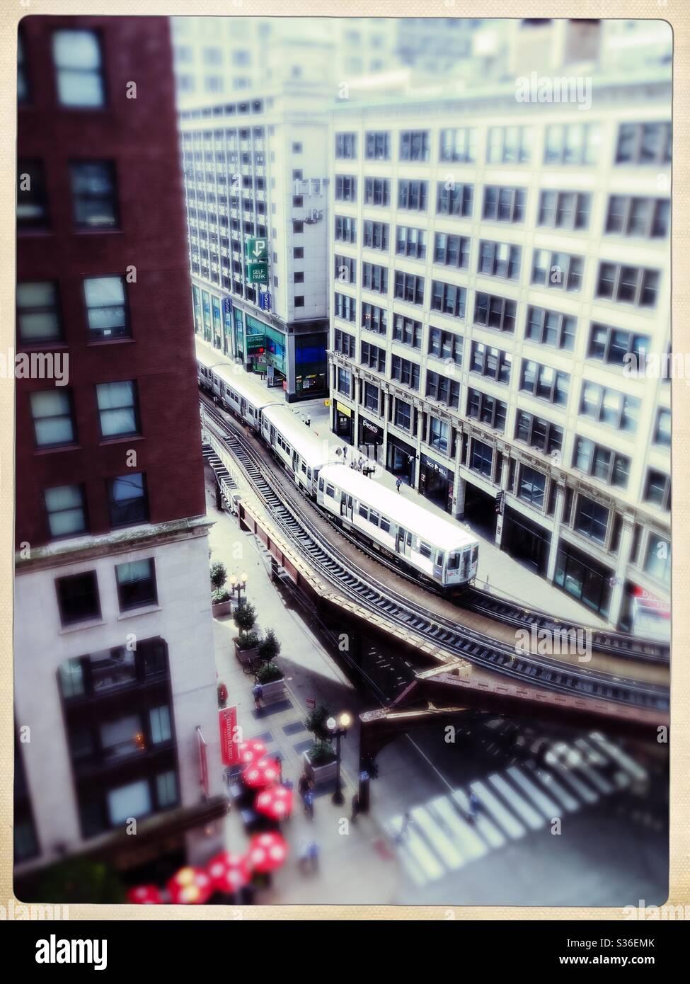 Guarda verso il basso un treno sopraelevato che attraversa un quartiere commerciale con edifici alti. Foto Stock