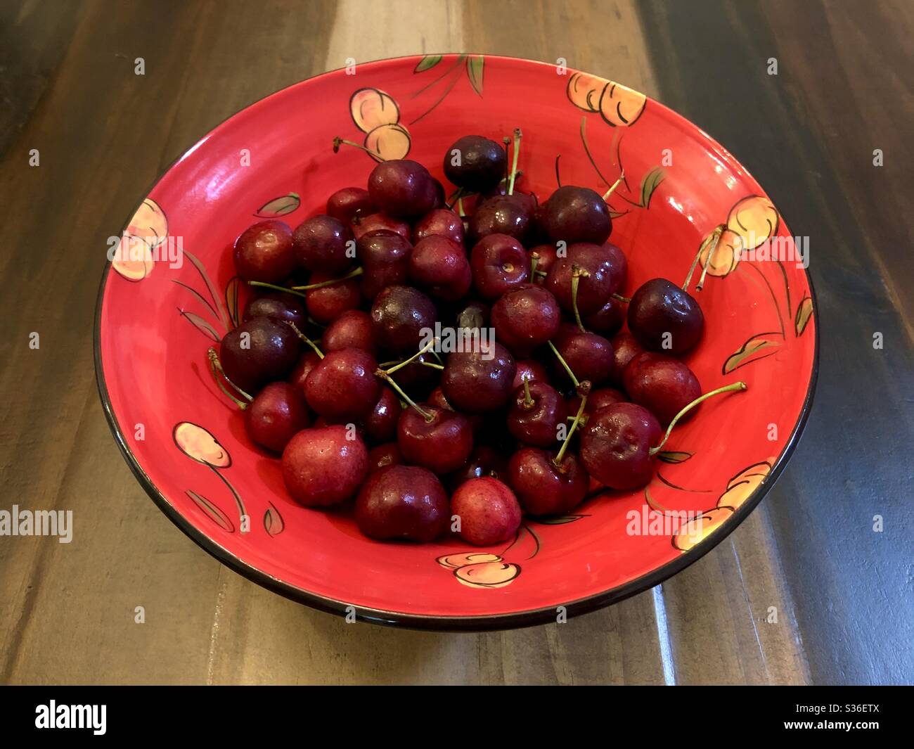 Ancora vita di una ciotola di ciliegie rosse in una ciotola di ceramica dipinta a mano con motivi di ciliegie. - Immagine stock catturata con smartphone