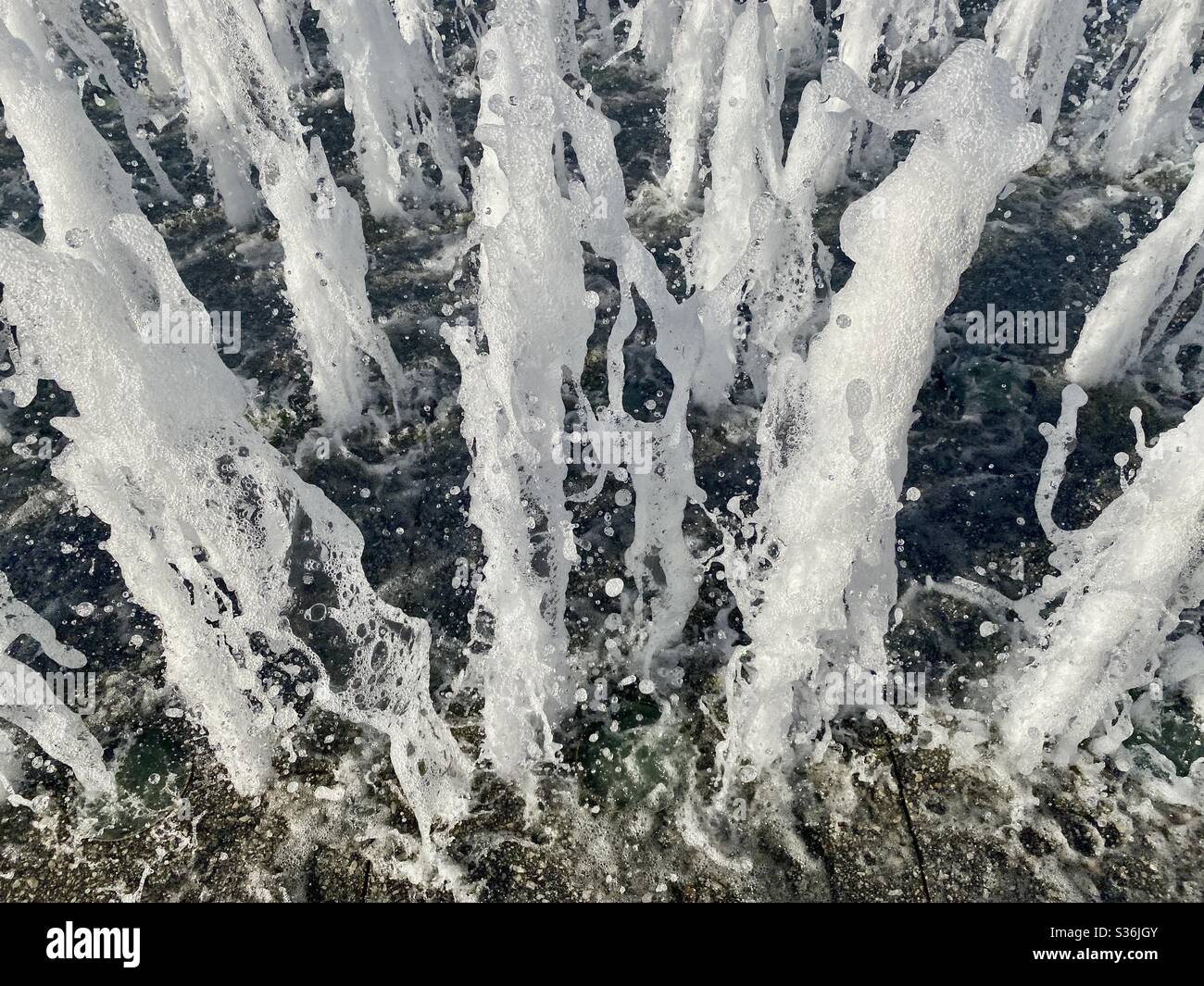 Vista dall'alto della fontana, spruzzatura verso la fotocamera, scatto con alta velocità dell'otturatore, sfondo scuro - Immagine stock catturata con smartphone