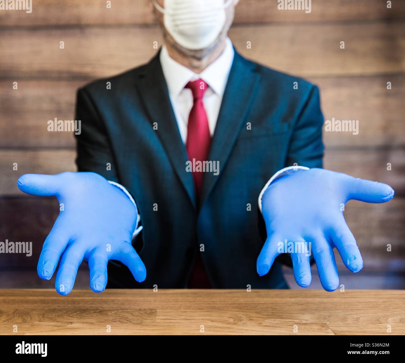 Un uomo d'affari, un medico o un datore di lavoro seduto su una scrivania con guanti chirurgici blu dpi e maschera facciale Foto Stock