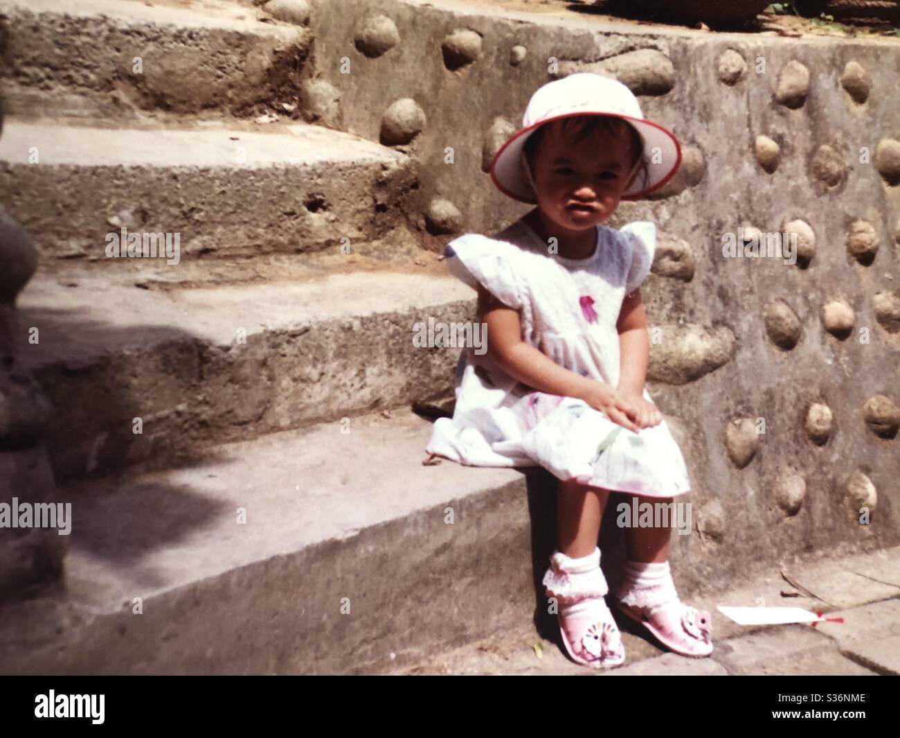 La bambina si siede accanto alla strada in una giornata calda Foto Stock