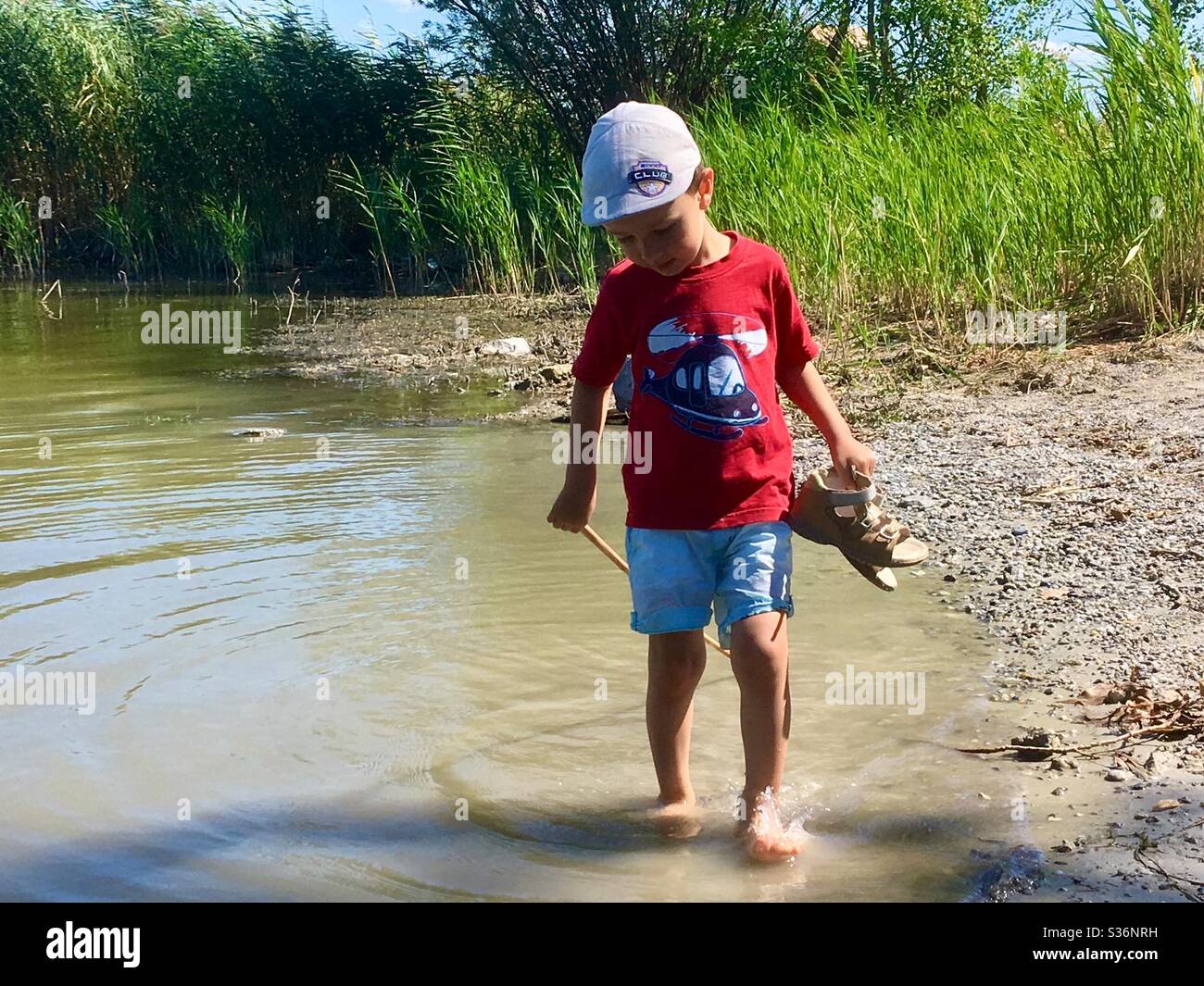 Bambino di 4 anni che si addormentava in acqua di lago tenendo i suoi sandali in estate, fermo-to, Fertorakos, Ungheria Foto Stock