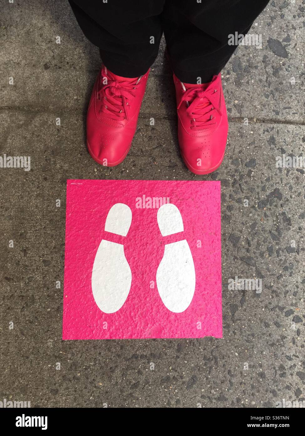 Immagine whimsical di una donna in scarpe rosa in piedi di fronte a un pittogramma rosa e bianco che sostiene la distanza sociale, New York, 2020 giugno, USA Foto Stock