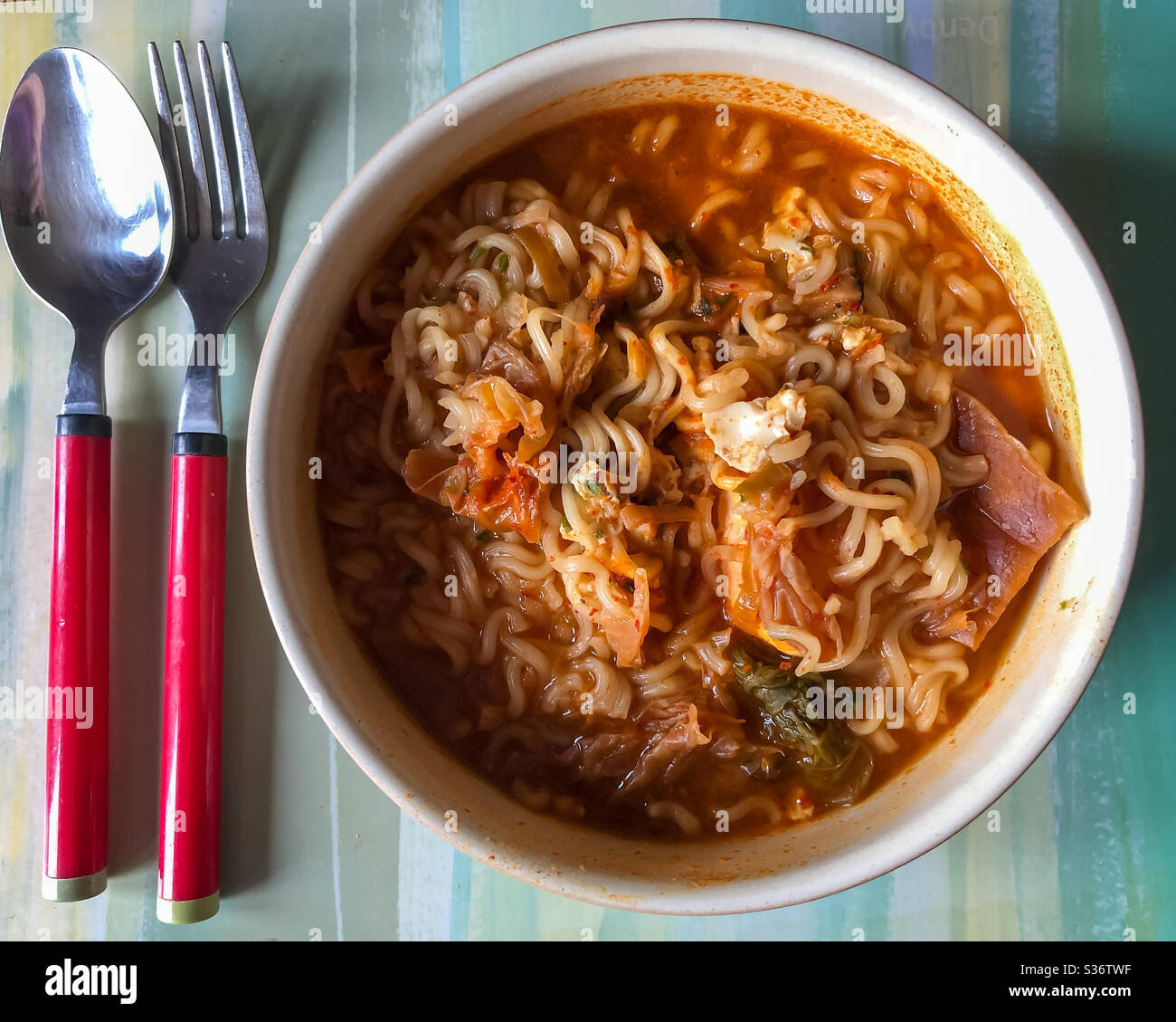 I noodle di sapore istantaneo di kimchi in una ciotola con forchetta e cucchiaio visto dall'alto. Pronto a mangiare per pranzo. Foto Stock