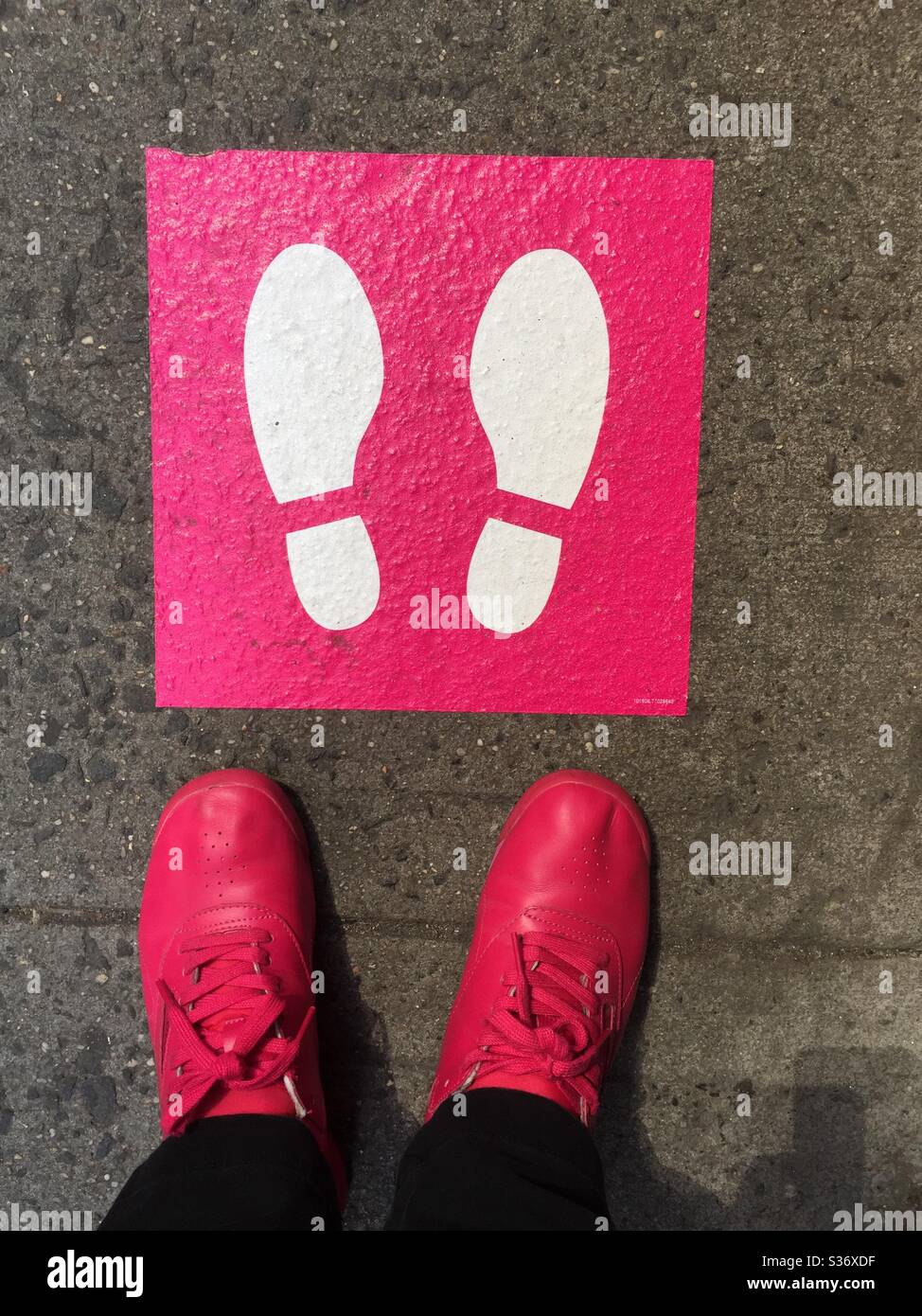 Immagine whimsical di una donna che si trova accanto ad un pittogramma sociale rosa e bianco a distanza con scarpe rosa corrispondenti durante la pandemia COVID-19, 2020, New York City, Stati Uniti Foto Stock