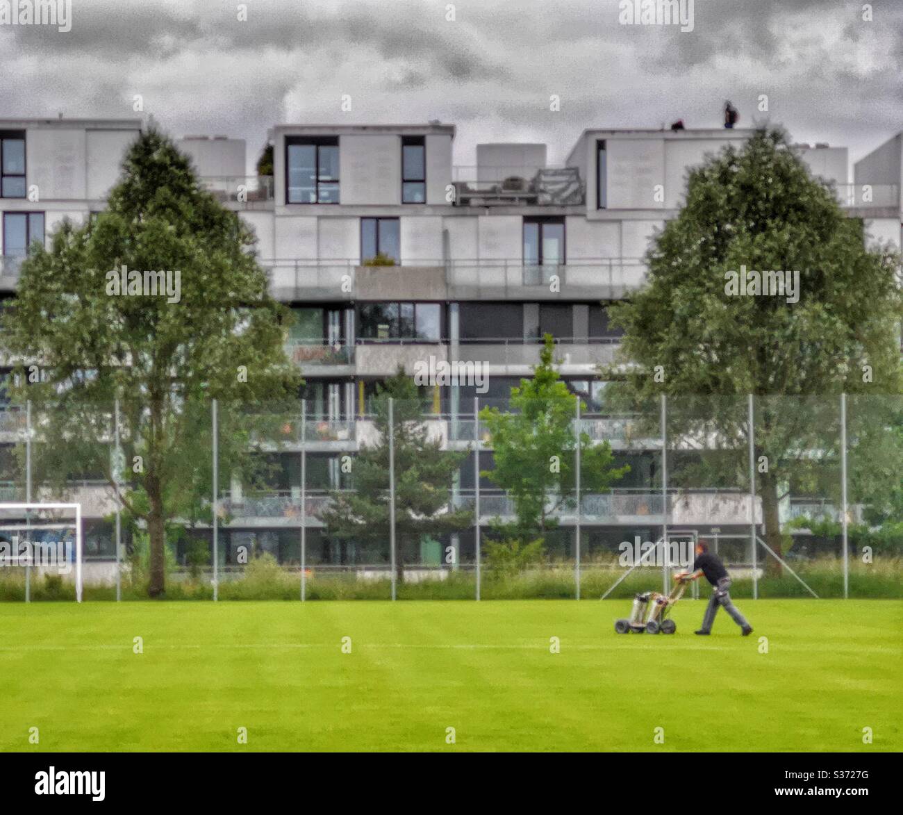 Uomo che dipinge linee sul campo da calcio con moderni edifici residenziali dietro - Immagine stock catturata con smartphone