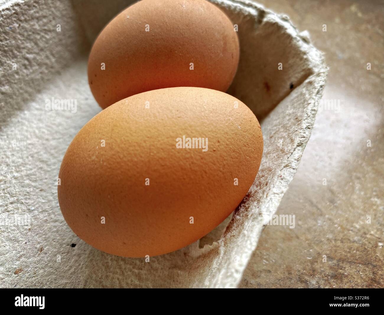 Vista closeup delle uova biologiche dell'allevamento in un cartone di cartone riciclabile tradizionale. Dettagli della scatola delle uova. Due uova in un vassoio sul banco della cucina. - Immagine stock catturata con smartphone
