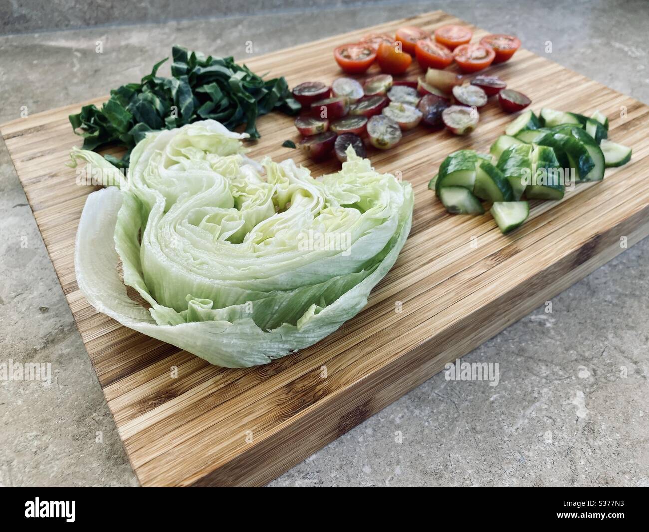 Vista dell'guardaroba su ingredienti per insalate preparati al momento per la cena. Uva rossa sana, lattuga, pomodori, cetriolo. Lavati e risciacquati. Affettato, tagliato e tagliato su un tritare di legno - Immagine stock catturata con smartphone