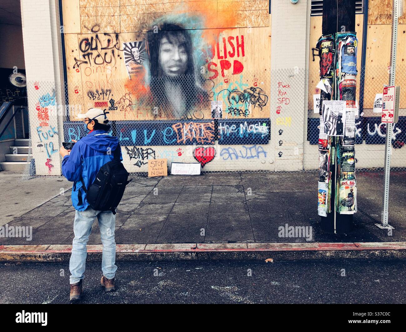 Un fotografo indipendente davanti a murales e graffiti sulla facciata salita del 12 ° distretto della polizia su Capitol Hill a Seattle, CHAZ Foto Stock