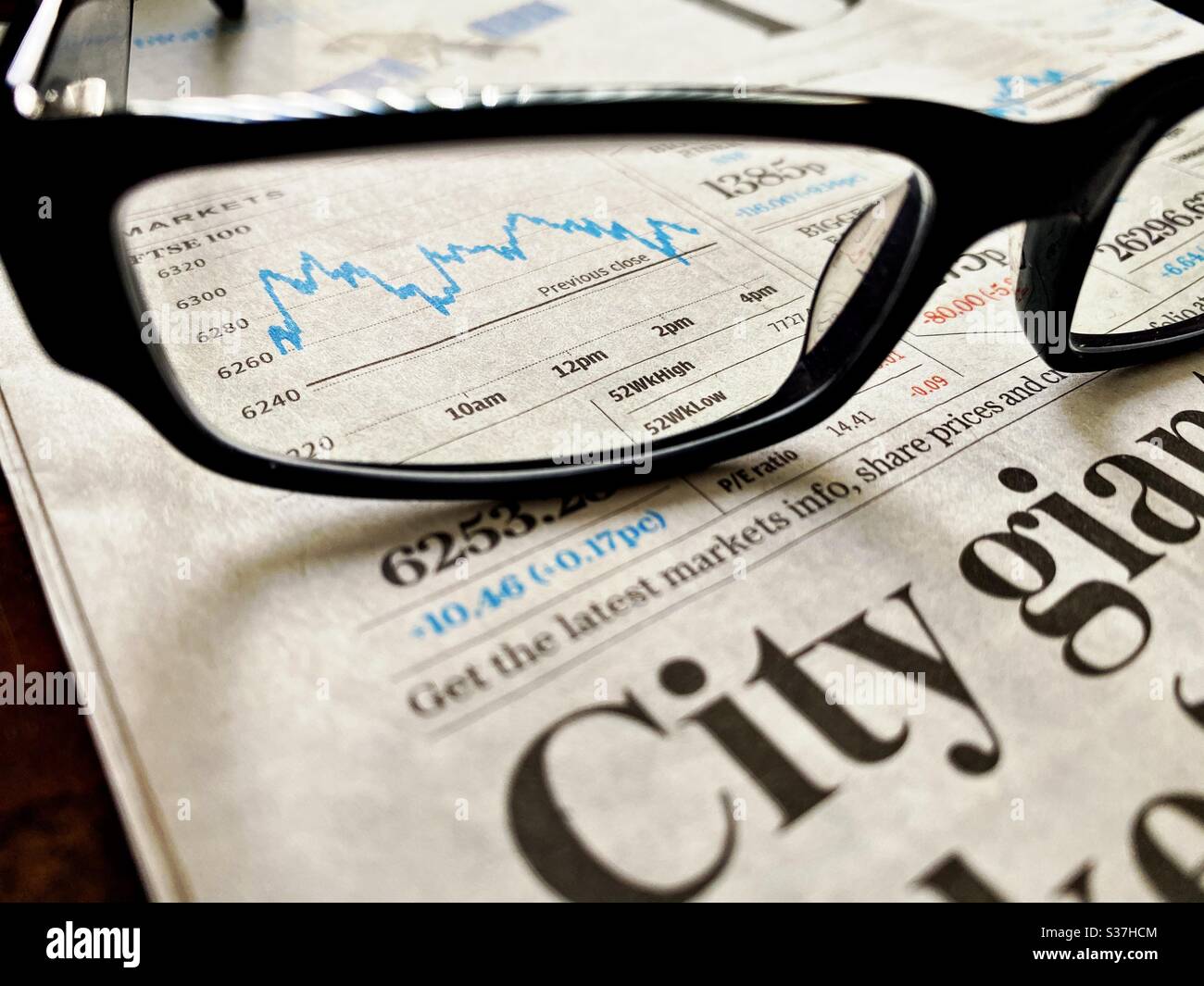 Concetto di business e finanza. Primo piano di un giornale finanziario con grafico che mostra i mercati di FTSE 100 in costante declino durante la crisi del coronavirus. Mercato crashing. Con occhiali da lettura - Immagine stock catturata con smartphone