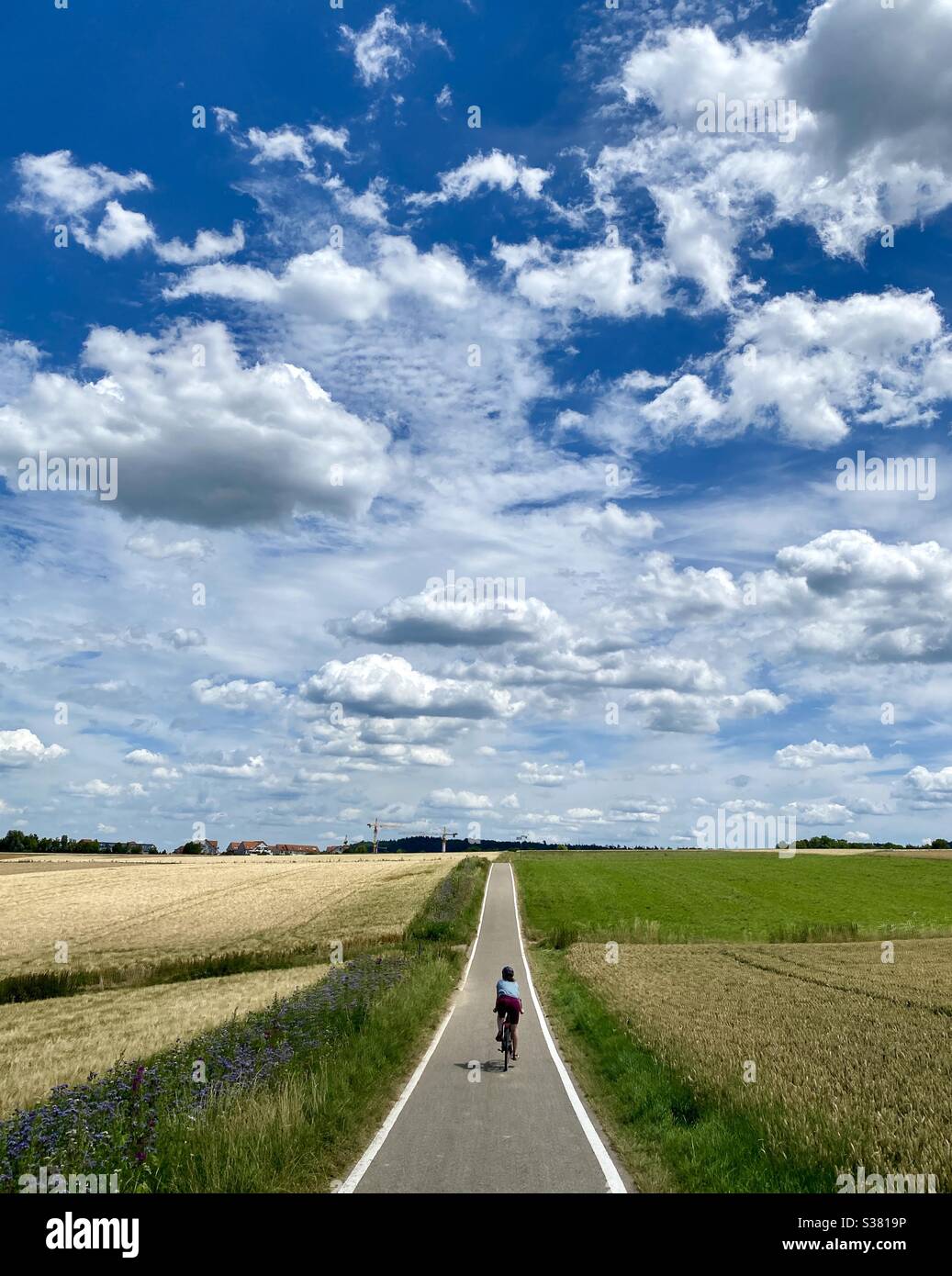 Una ragazza che cavalcava una bicicletta nei campi sotto il cielo nuvoloso drammatico, Stoccarda, Germania Foto Stock