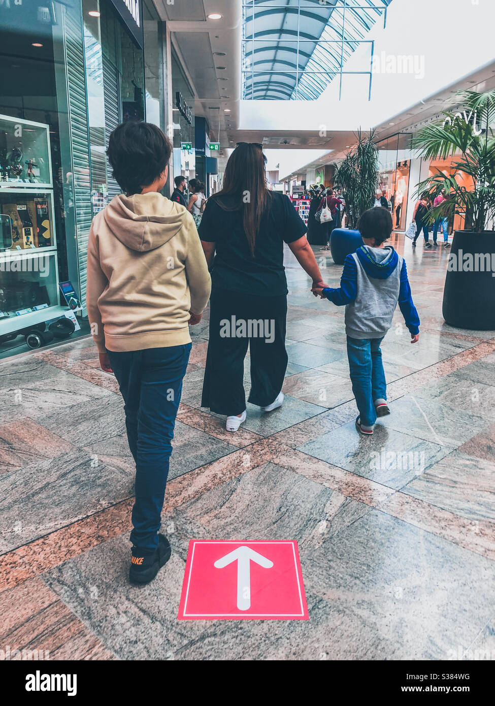 Una famiglia segue un sistema a senso unico in un centro commerciale. Il sistema unidirezionale è quello di supportare la distanza sociale come conseguenza di COVID-19. Foto Stock