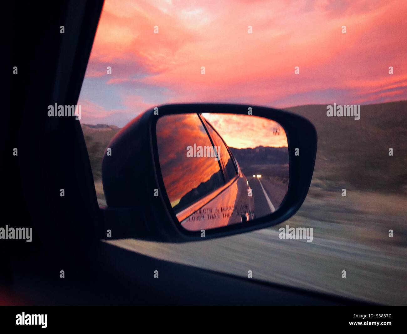 Tramonto fiammeggiante che si riflette nello specchio retrovisore laterale dell'auto sulla strada dal Death Valley National Park in California Foto Stock