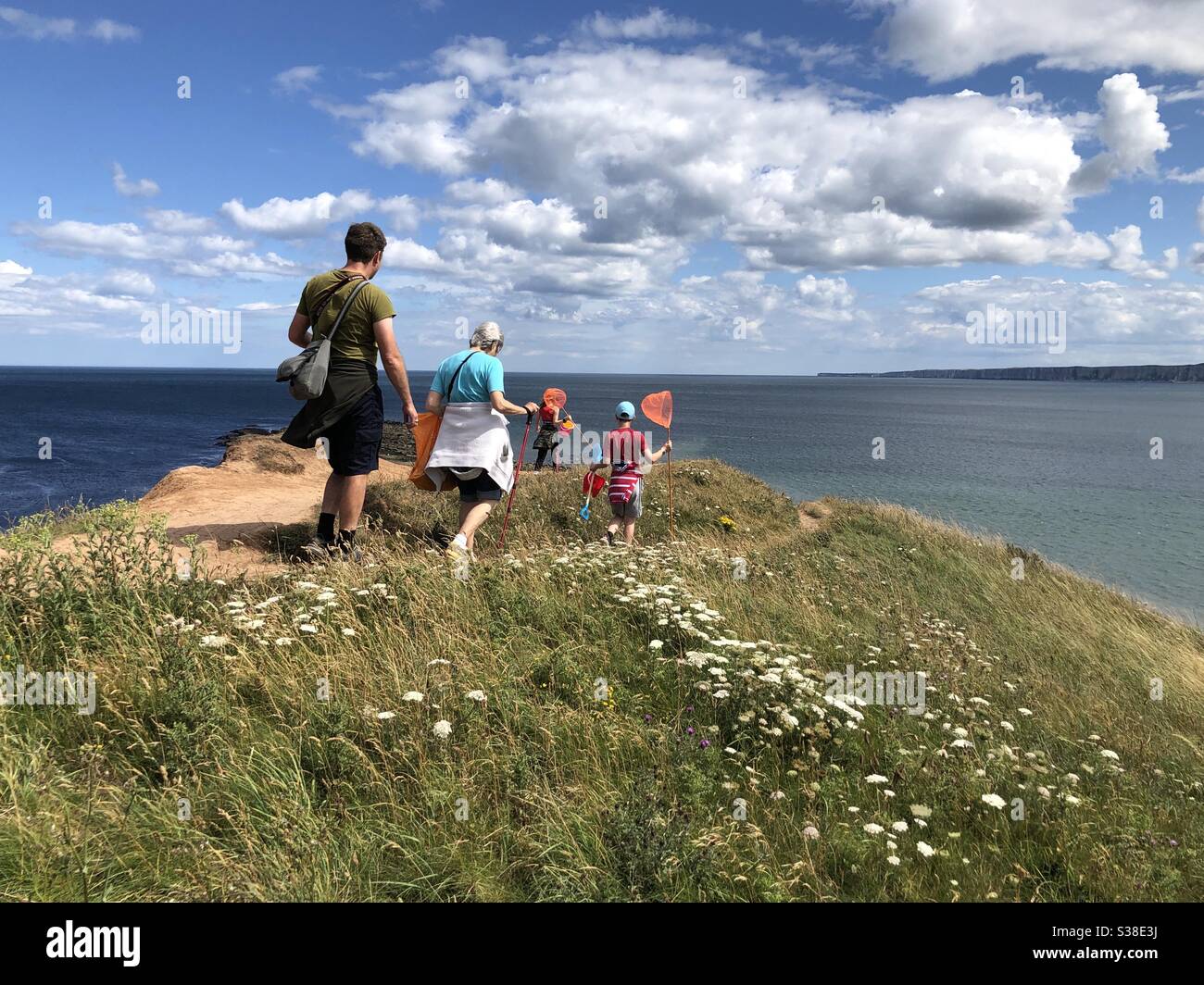 Felice famiglia che porta reti da pesca giù per la scogliera al mare Foto Stock