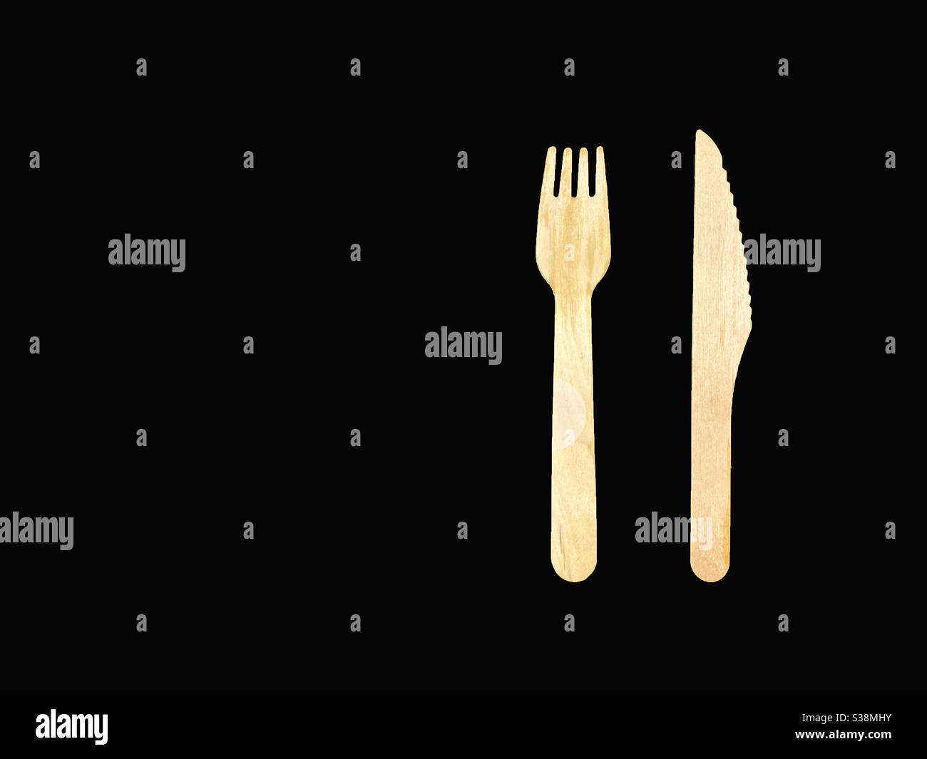 Coltello di legno e forchetta sfalsati a destra su uno sfondo nero semplice, nessuna gente. Spazio per la copia a sinistra. Foto Stock