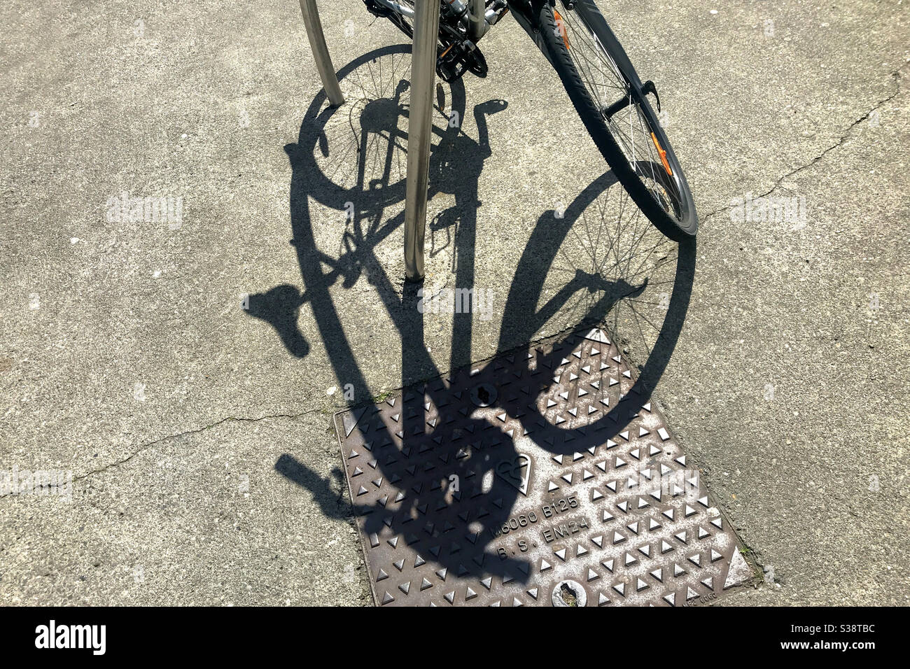 L'ombra della bicicletta sul marciapiede e la copertura del tombino da portabiciclette parcheggio - Immagine stock catturata con smartphone