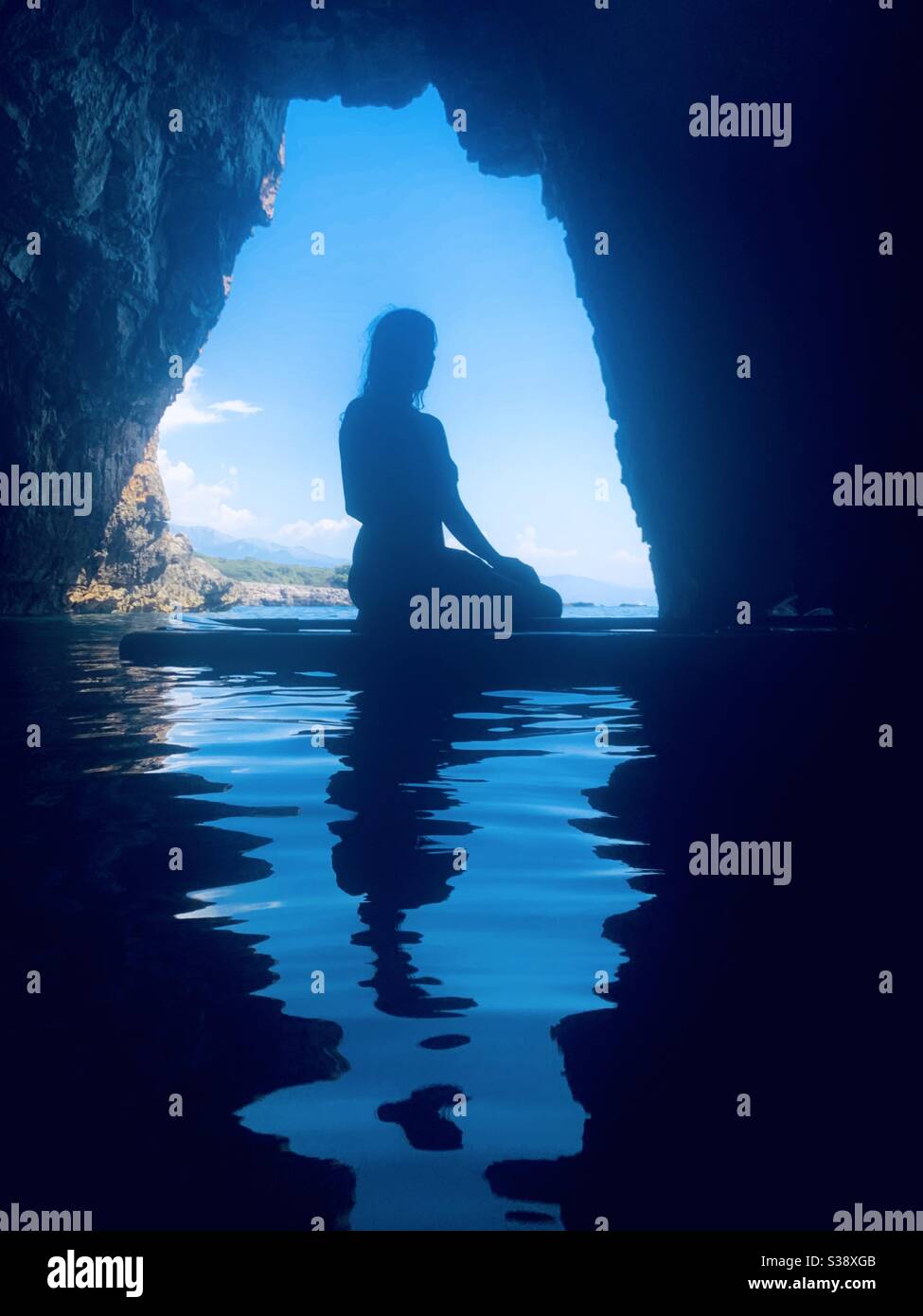 Silhouette di donna seduta su tavola a pale alla bocca di grotta - Immagine stock catturata con smartphone