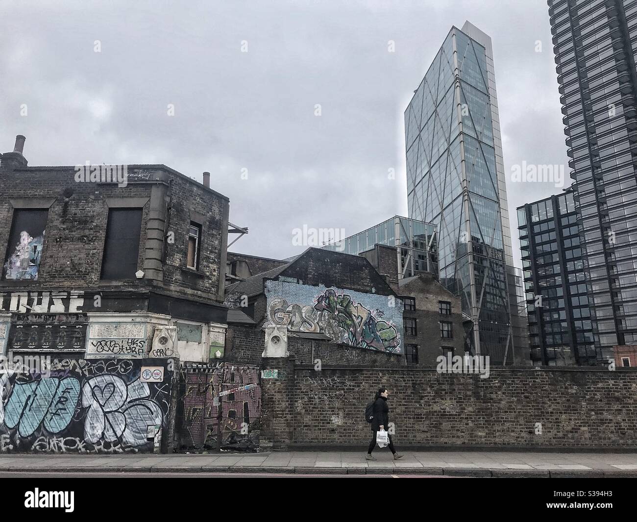 Lady camminando lungo la strada di Londra con un muro di graffiti e alto edifici in background e colore desaturato Foto Stock