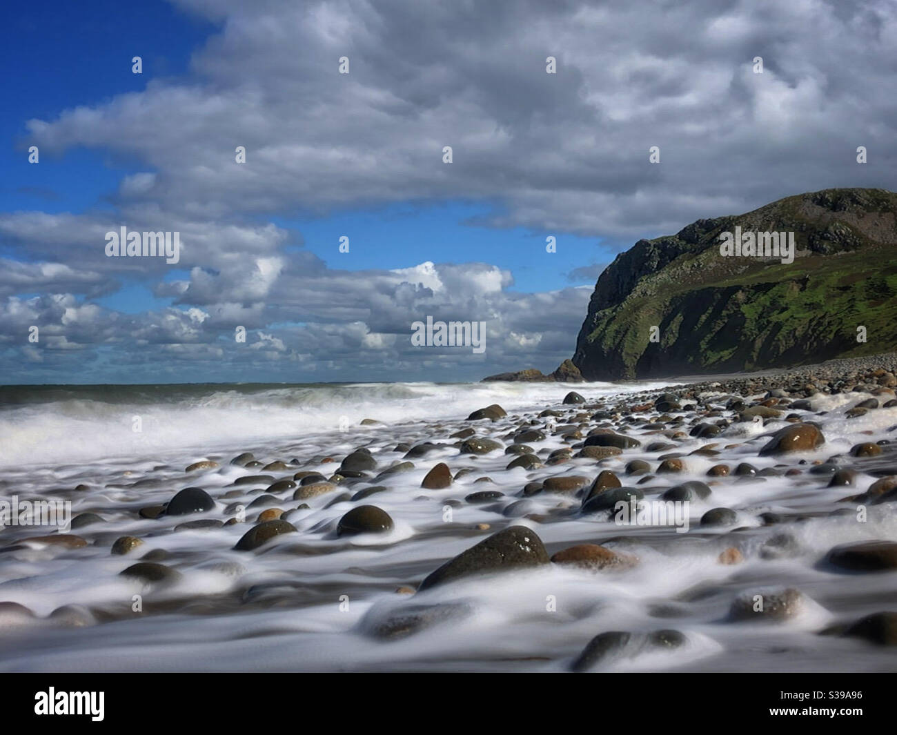 Onde che si infrangono sulla spiaggia di Pistyll, con il promontorio di Penryn Glas, Galles del Nord Foto Stock