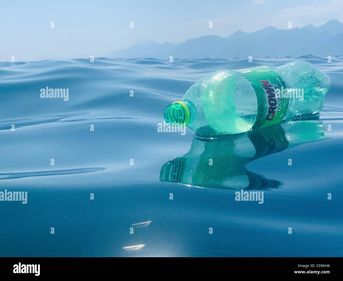 Bottiglia di plastica verde che galleggia su un mare blu - Immagine stock catturata con smartphone