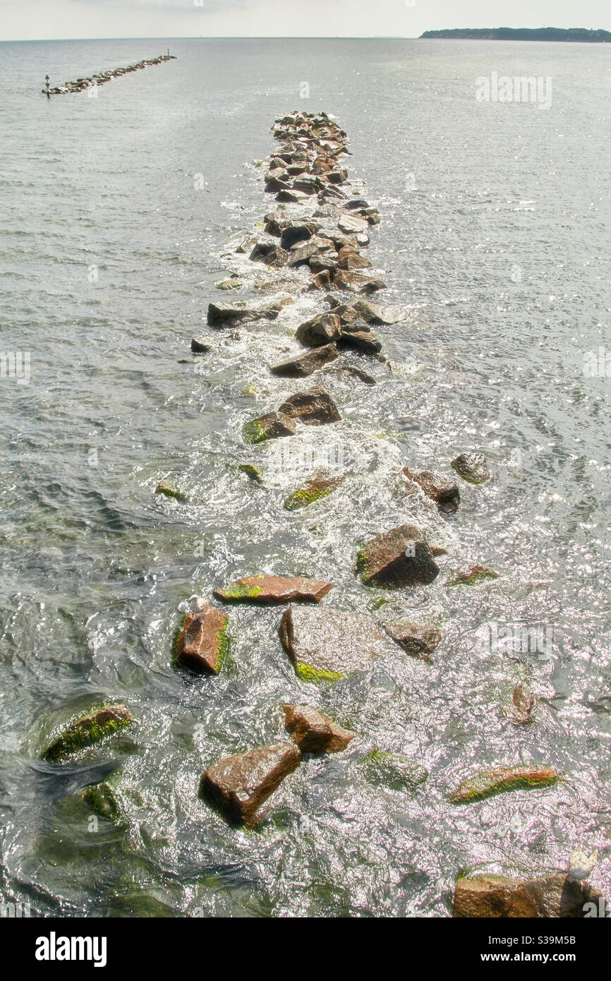 Due frangiflutti in pietra e roccia, allagati da acqua di mare, alghe verdi e alghe marine, al largo della costa del Mar Baltico Foto Stock