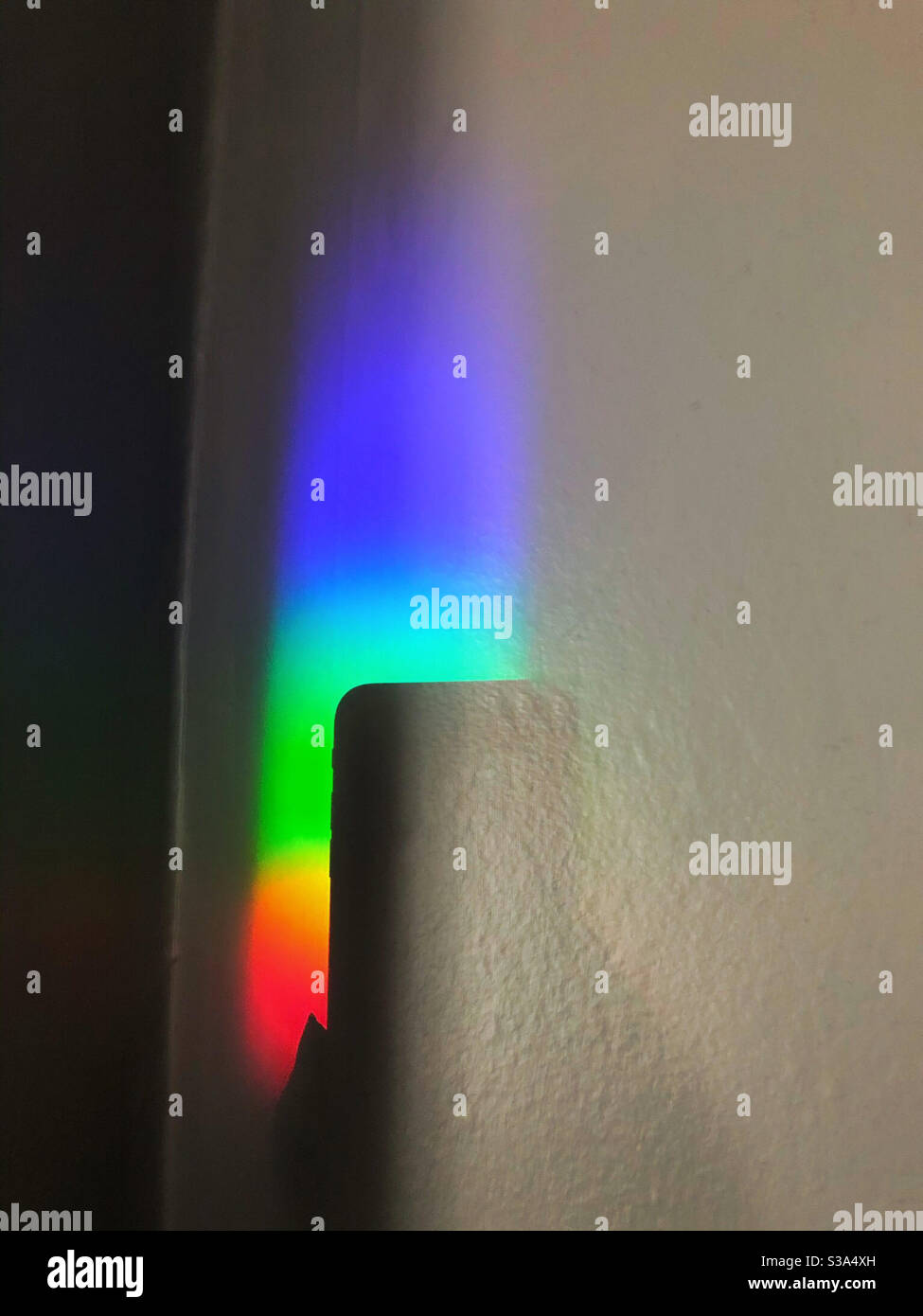 La donna fotografa il prisma dell'arcobaleno utilizzando la fotocamera dello smartphone, mostrata dall'ombra, all'interno della casa Foto Stock