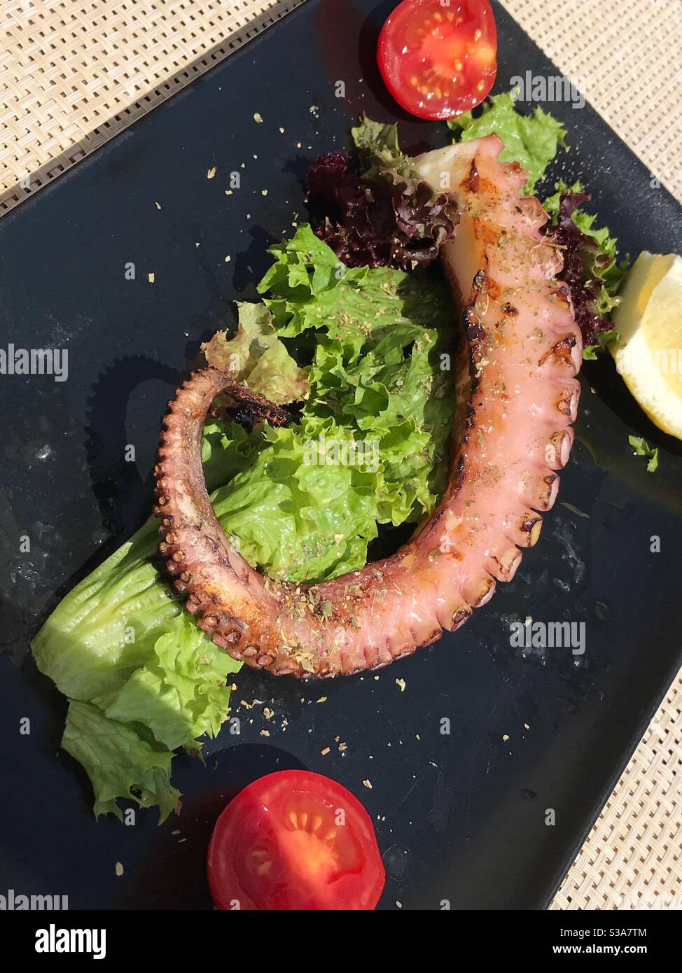 Piatto nero con polpo alla griglia e pomodori Foto Stock