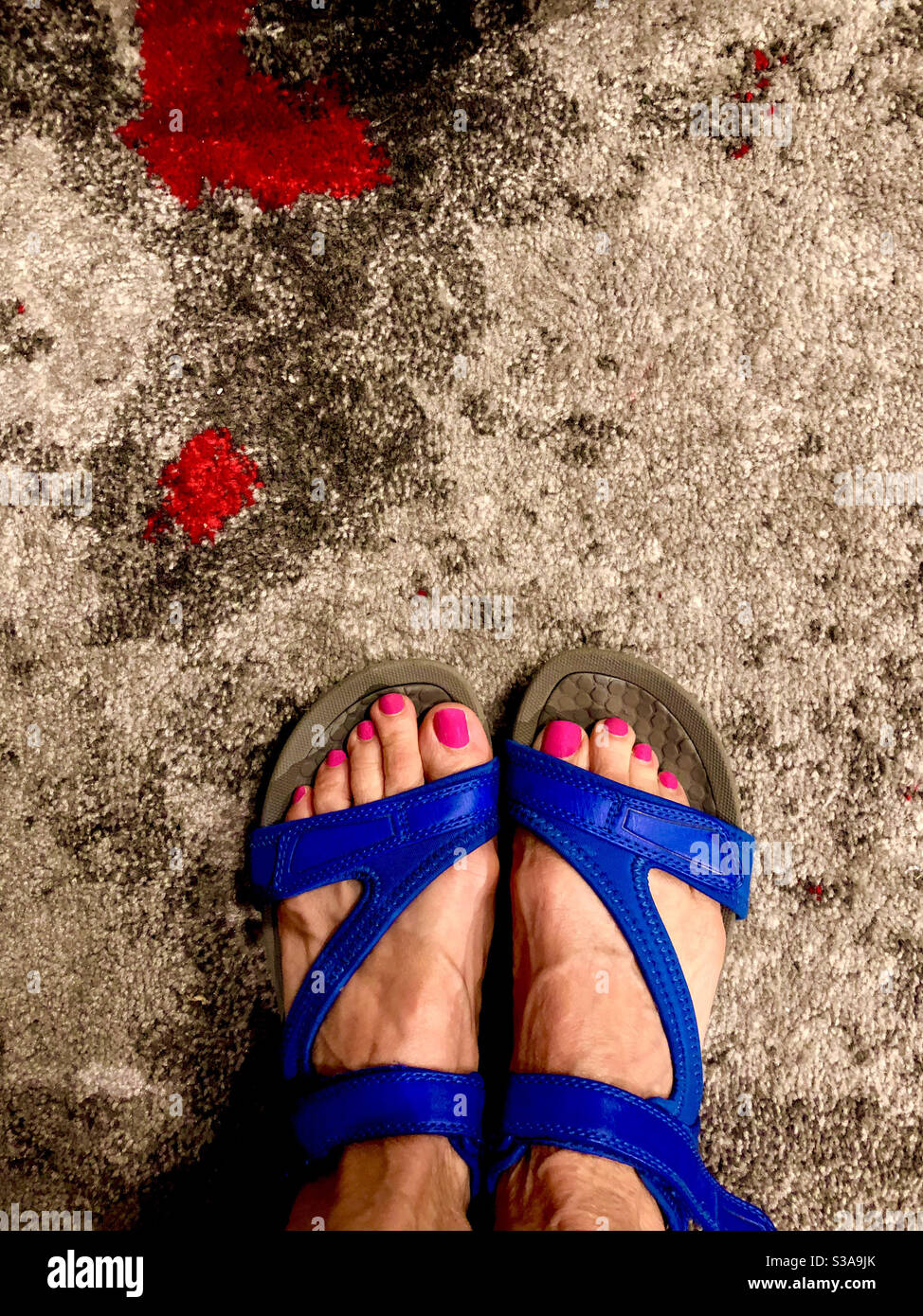 Unghie rosa in sandali blu - piedi in piedi su un tappeto. Foto Stock